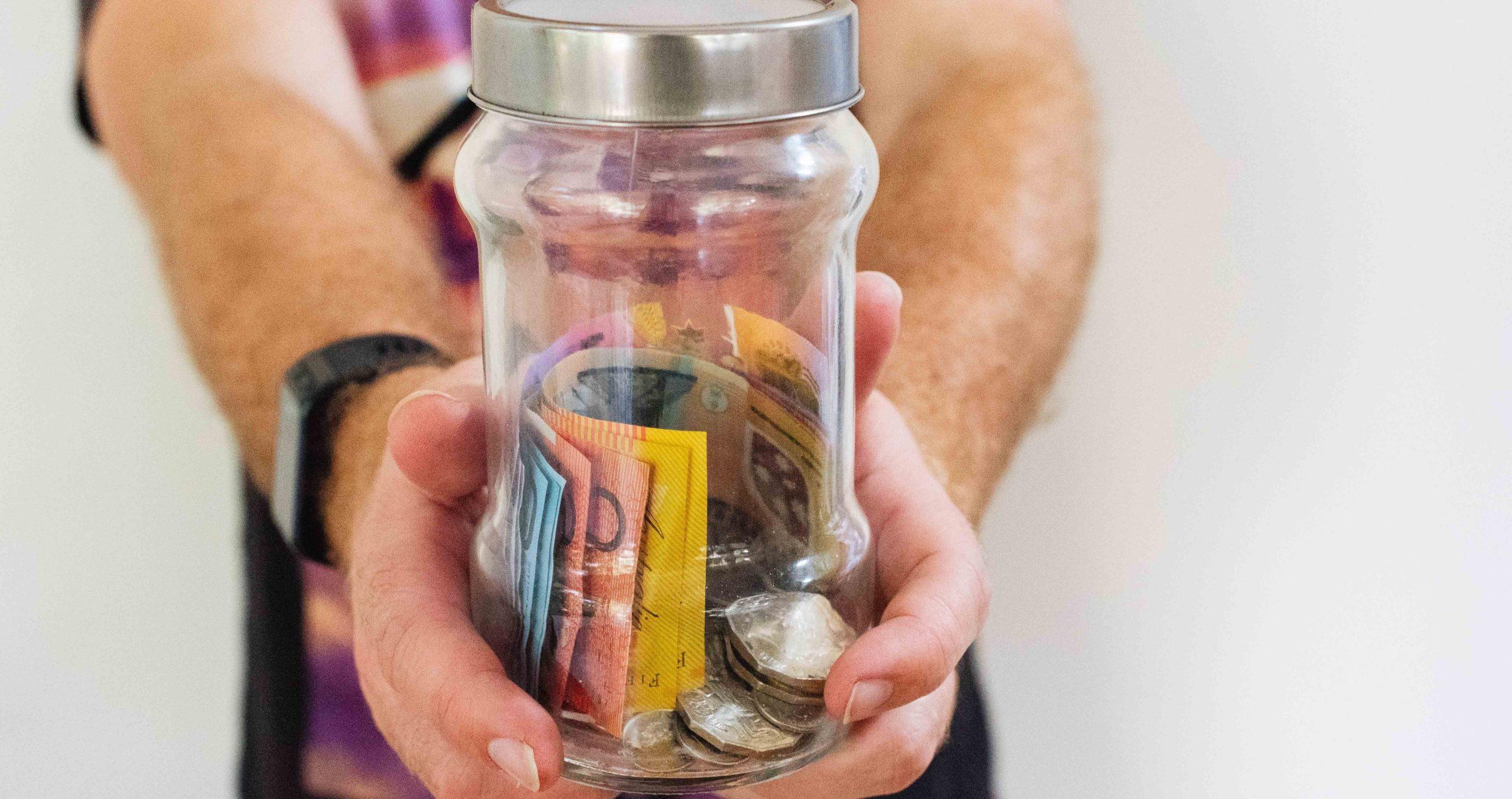 Person holding a jar filled with Australian currency.