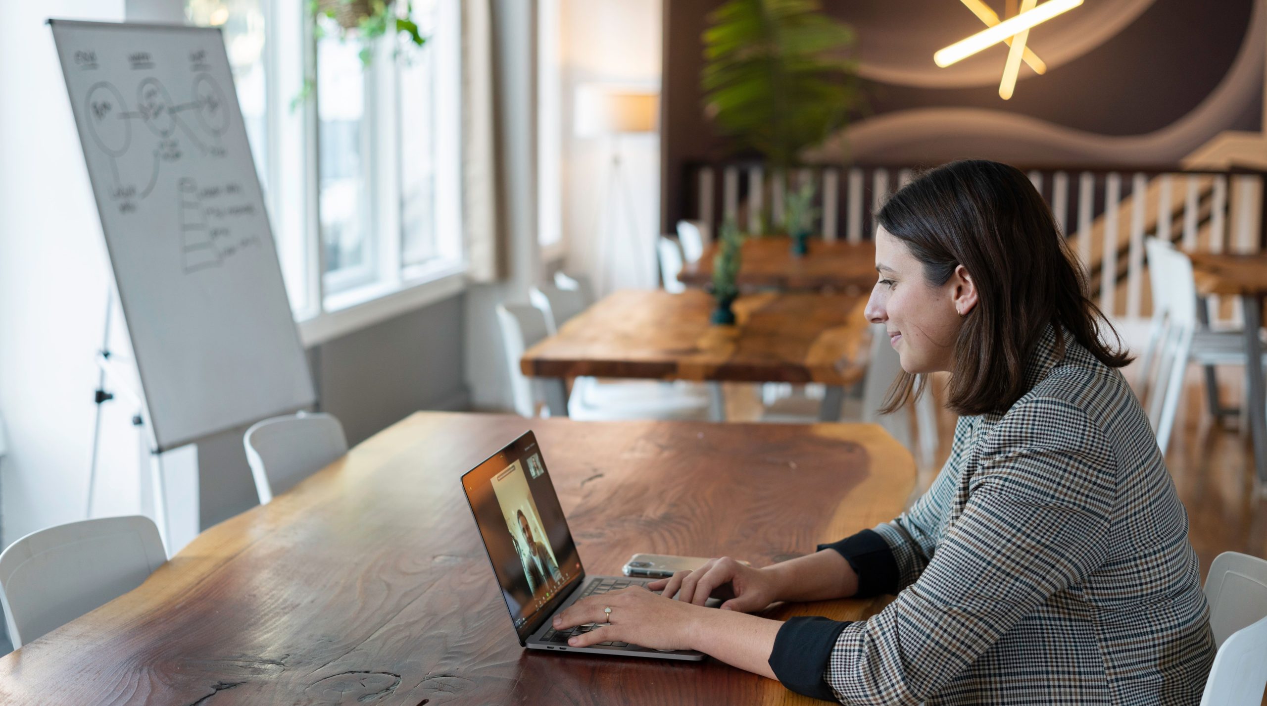 Woman sitting in front of a laptop in an office-like setting during a video call.