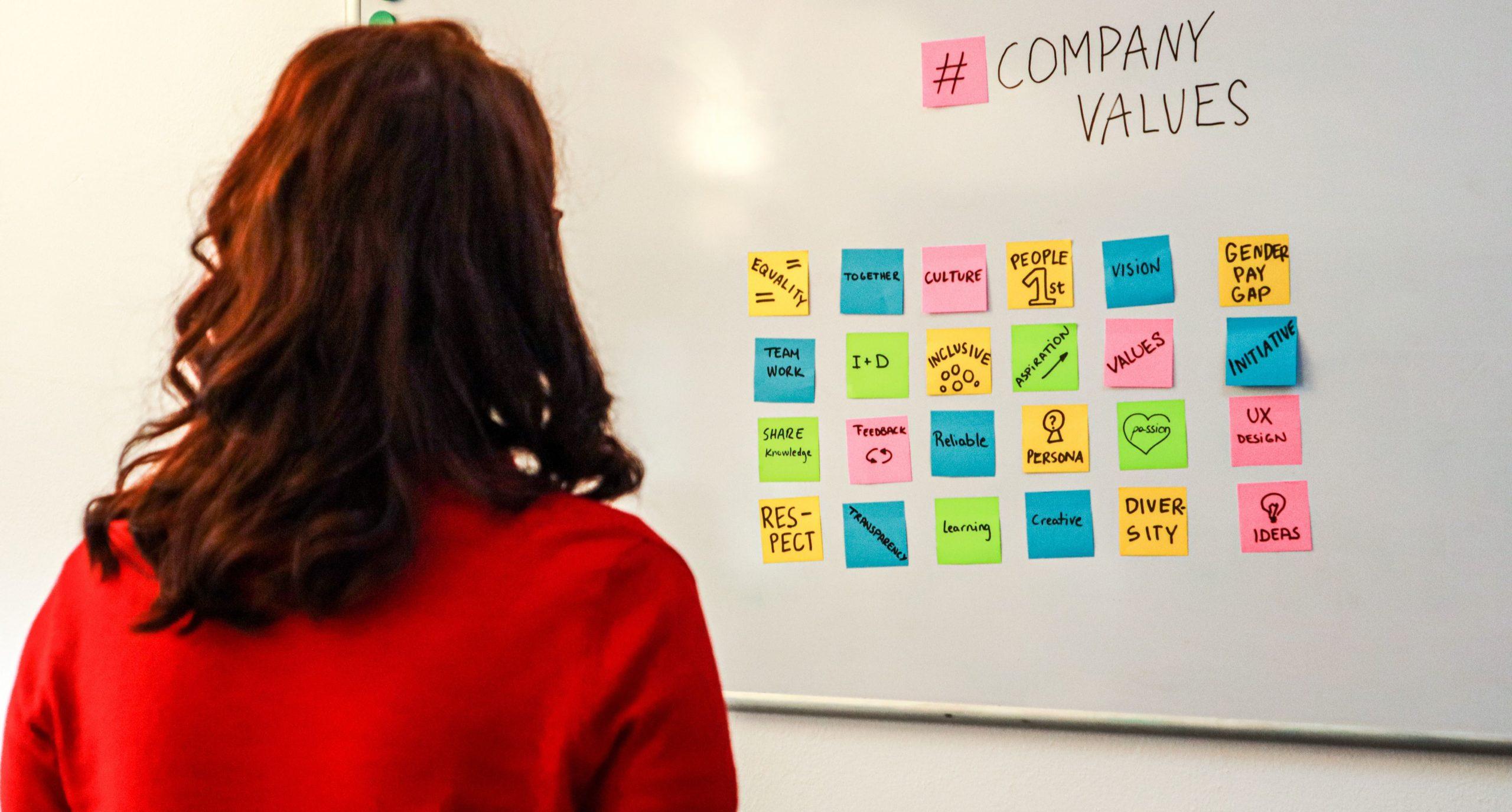 Woman looking at a whiteboard with post-it notes showing company values.