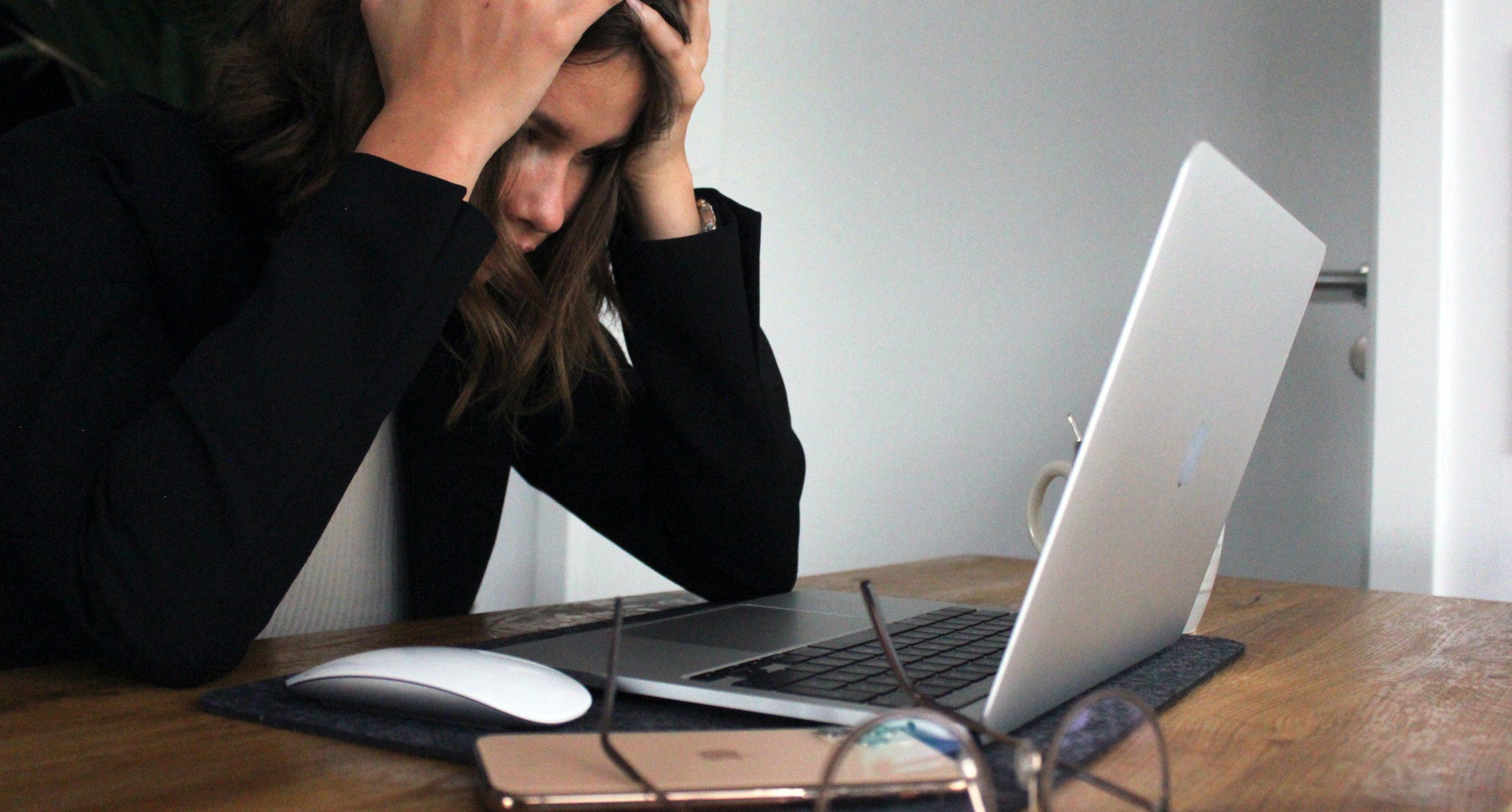 Woman sitting at desk in front of a laptop looking stressed.