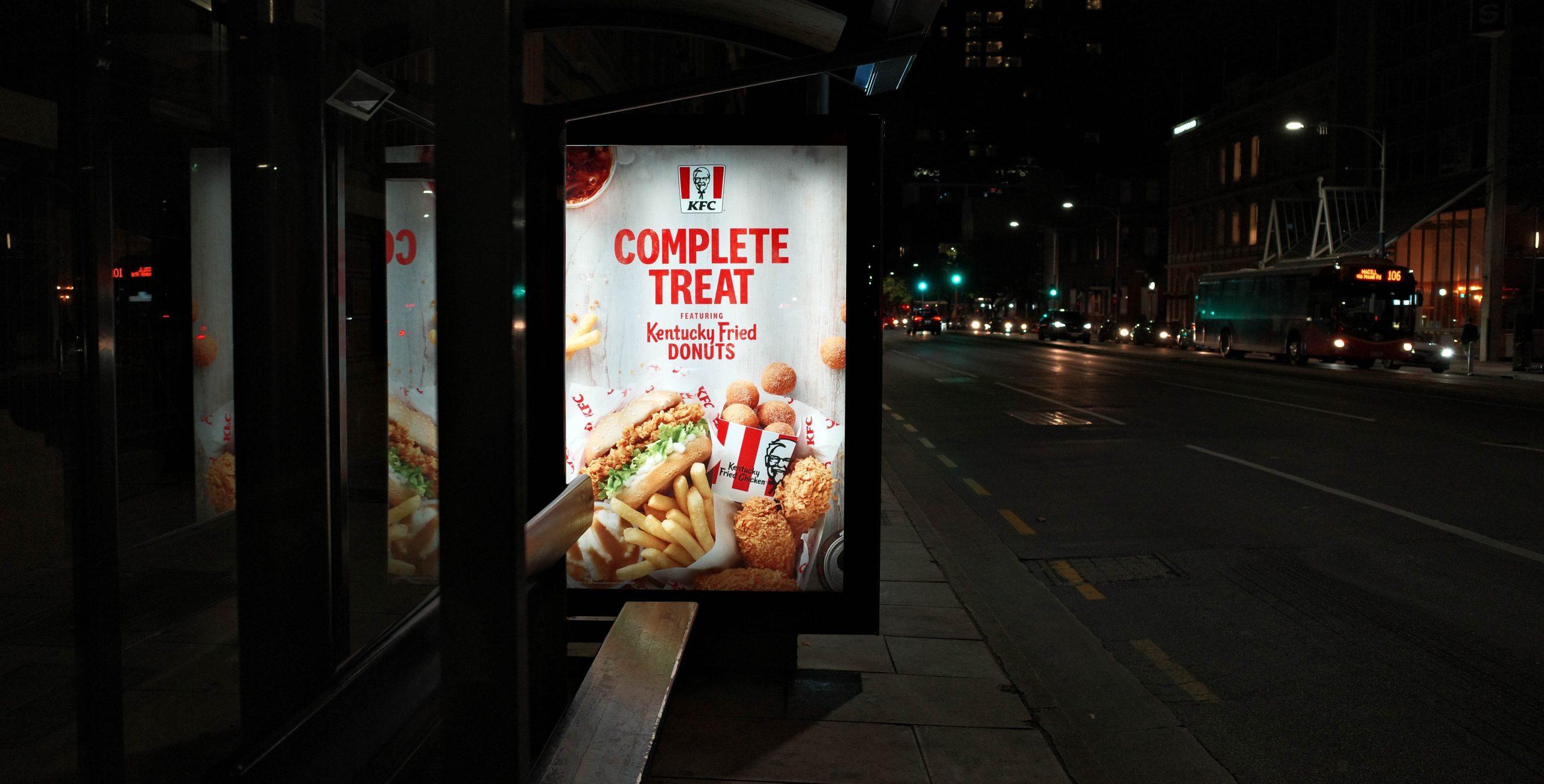 Illuminated KFC ad at a bus stop.