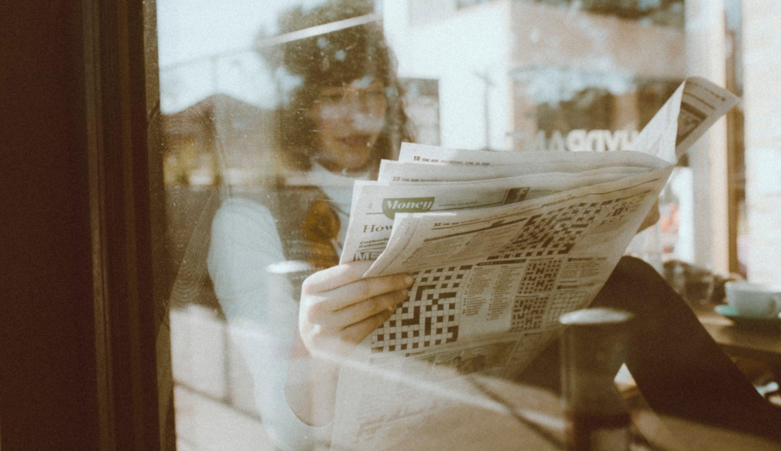Woman sitting down reading a newspaper.