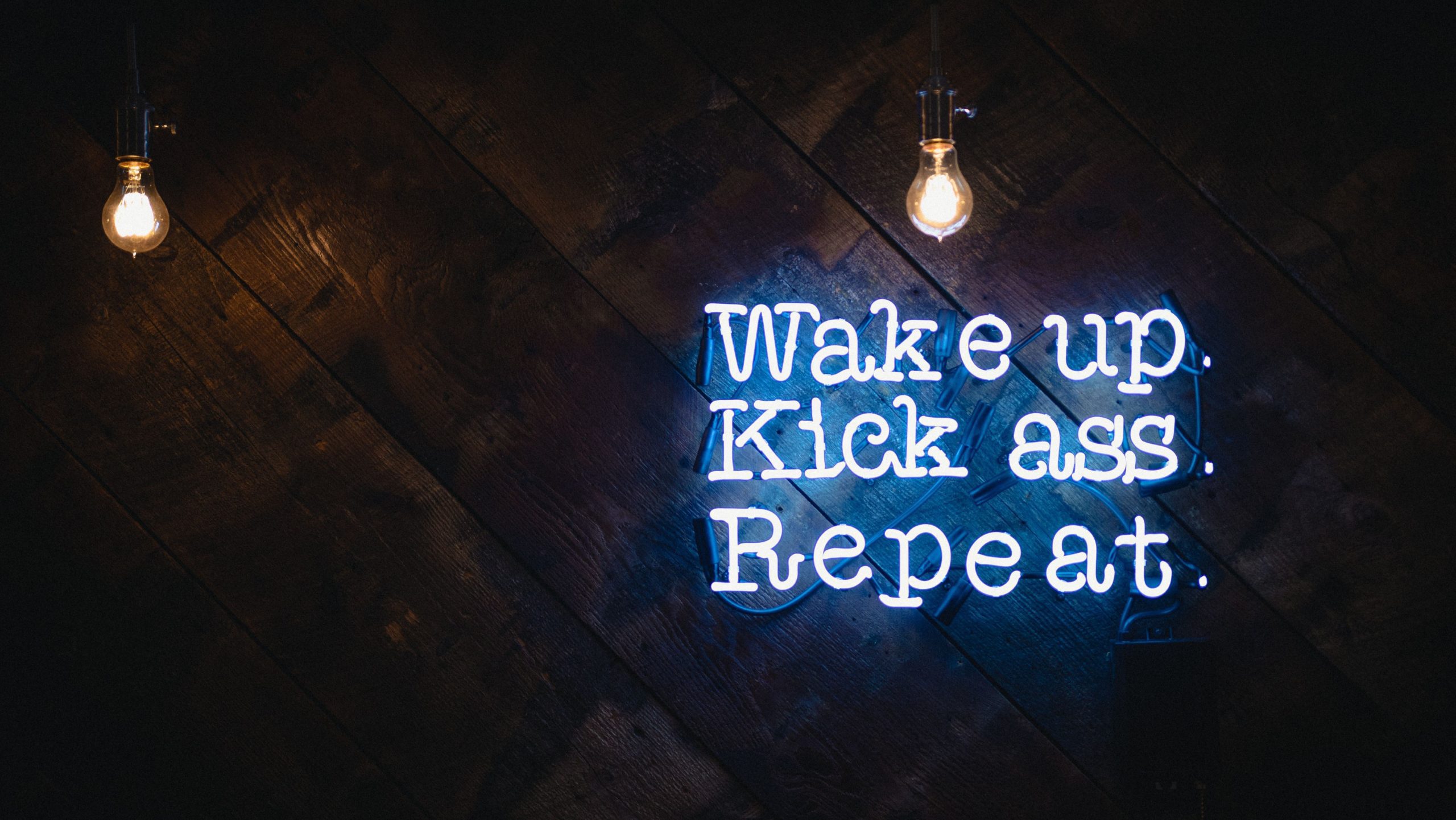Illuminated sign with the words 'wake up, kick ass, repeat'.