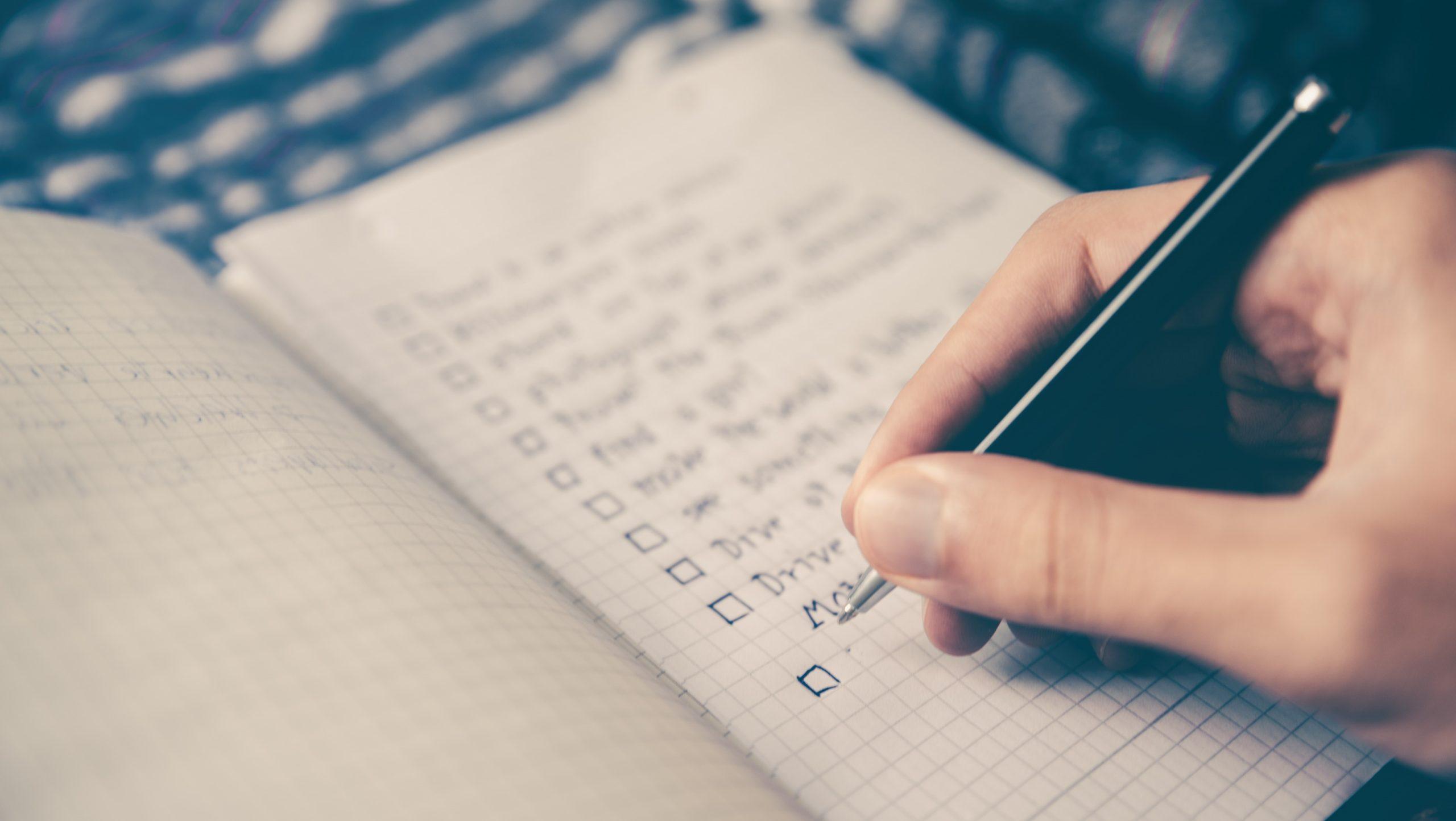 Person writing in a notepad as part of an article about a marketing checklist.