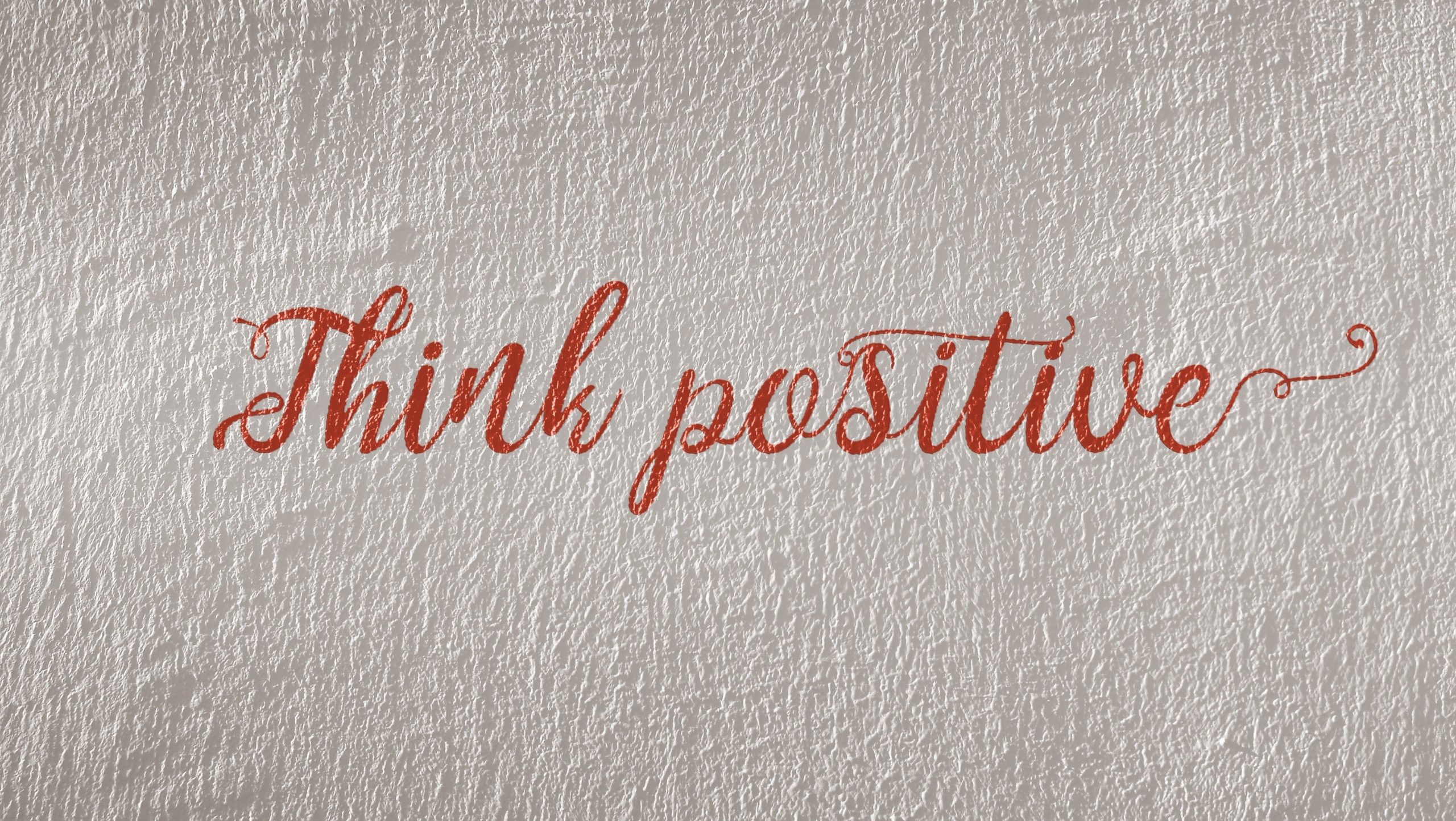 Red cursive writing that spells the words, 'Think positive'.