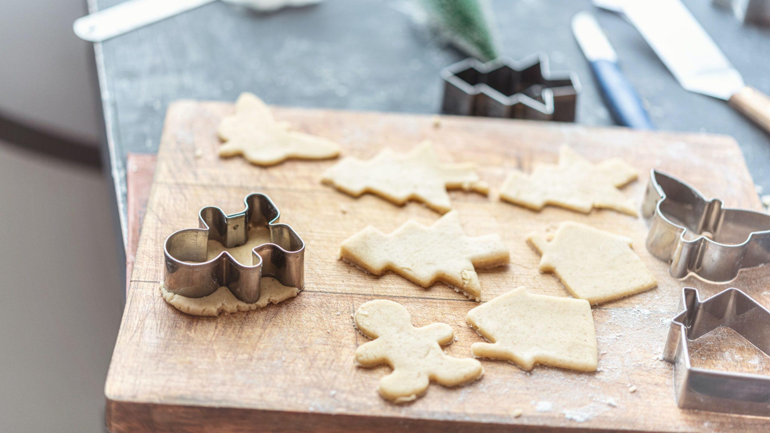 Unbaked cookies and cookie cutters placed on a wooden chopping board. 