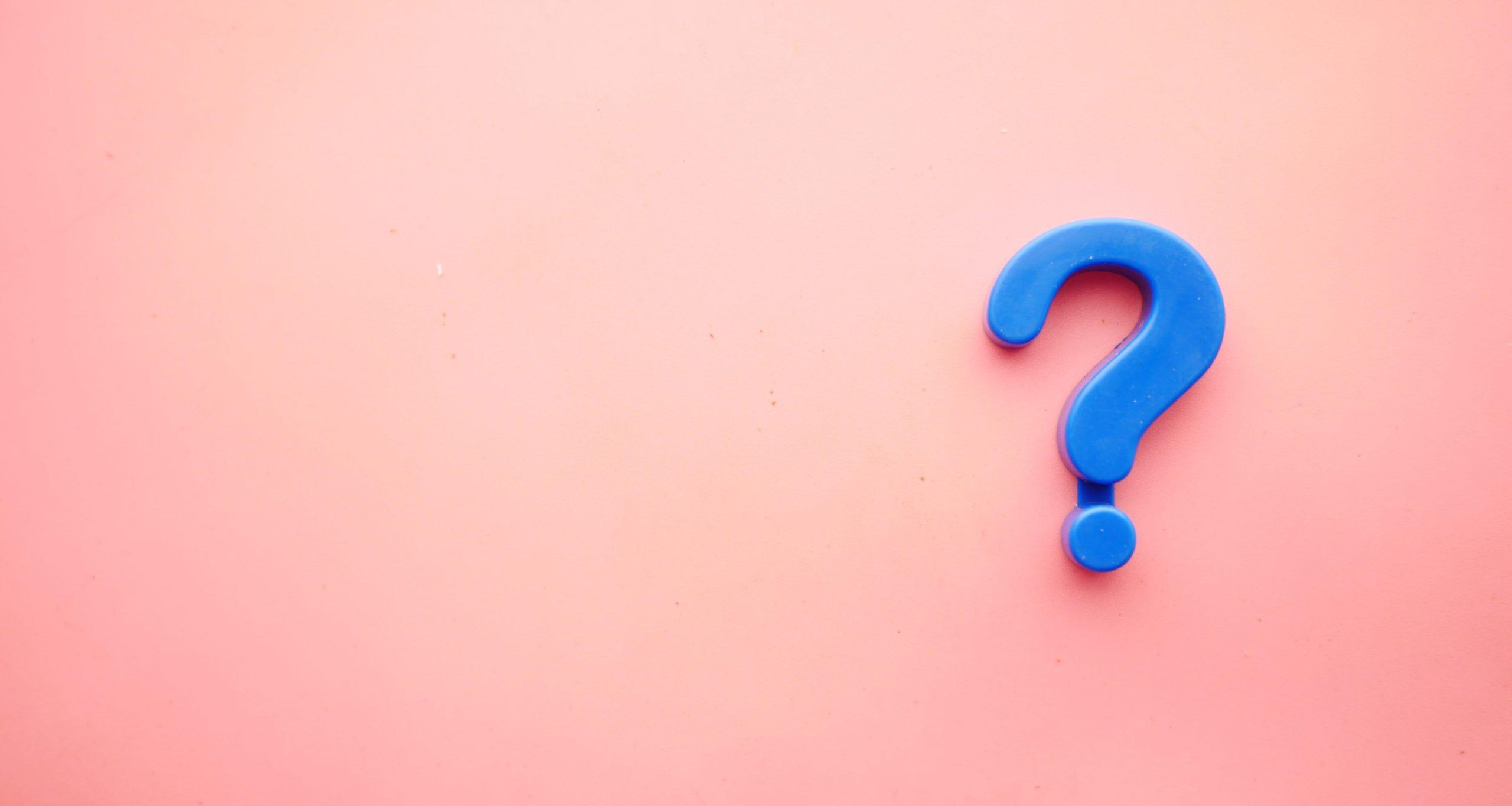 A blue-coloured question mark against a pinkish background.