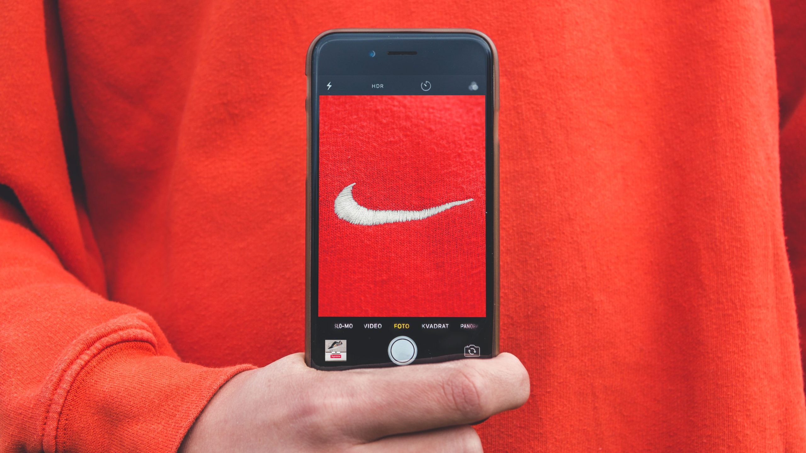Person wearing a red jumper holding a smartphone with the Nike logo.