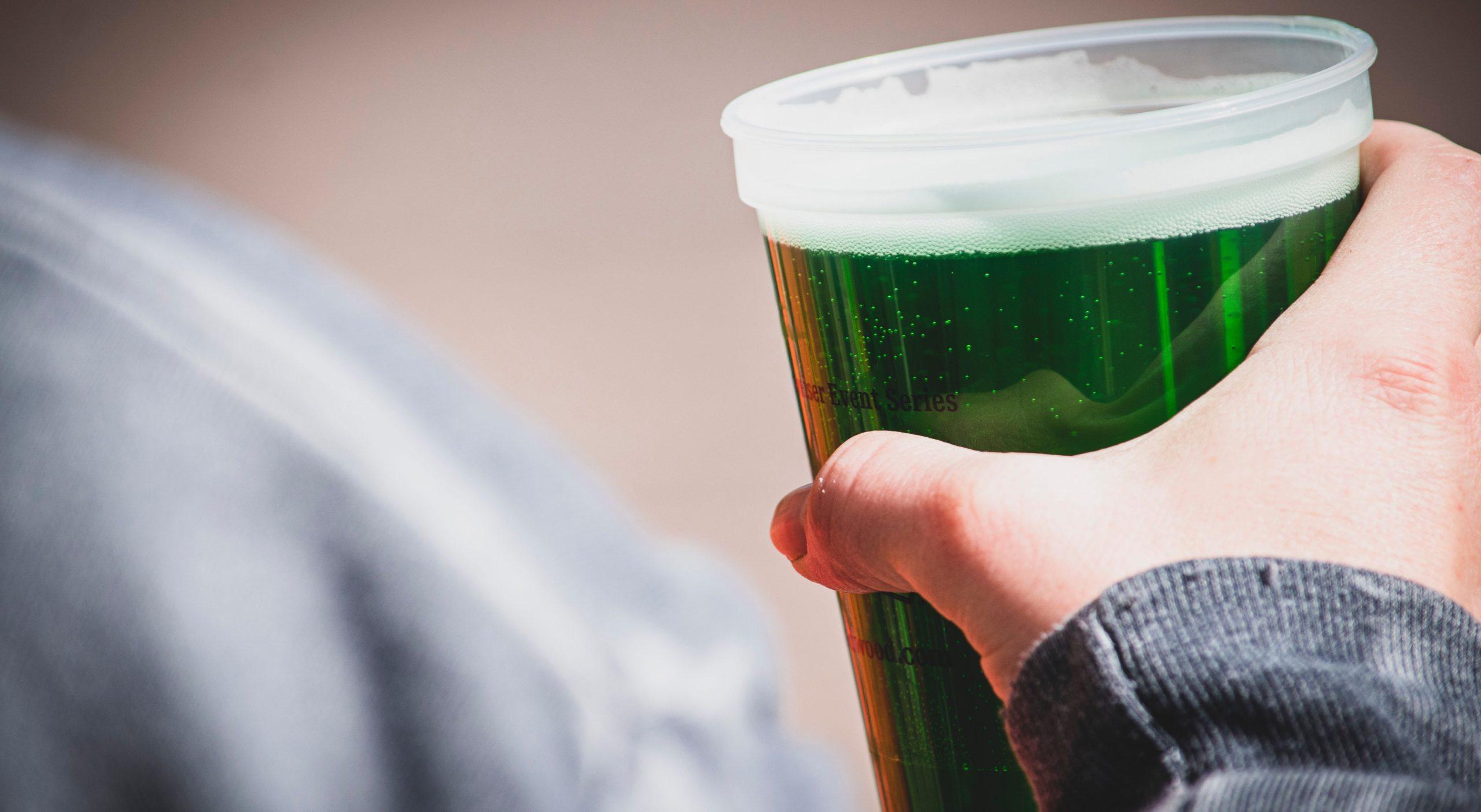 Close up of a person holding a green-coloured beer.
