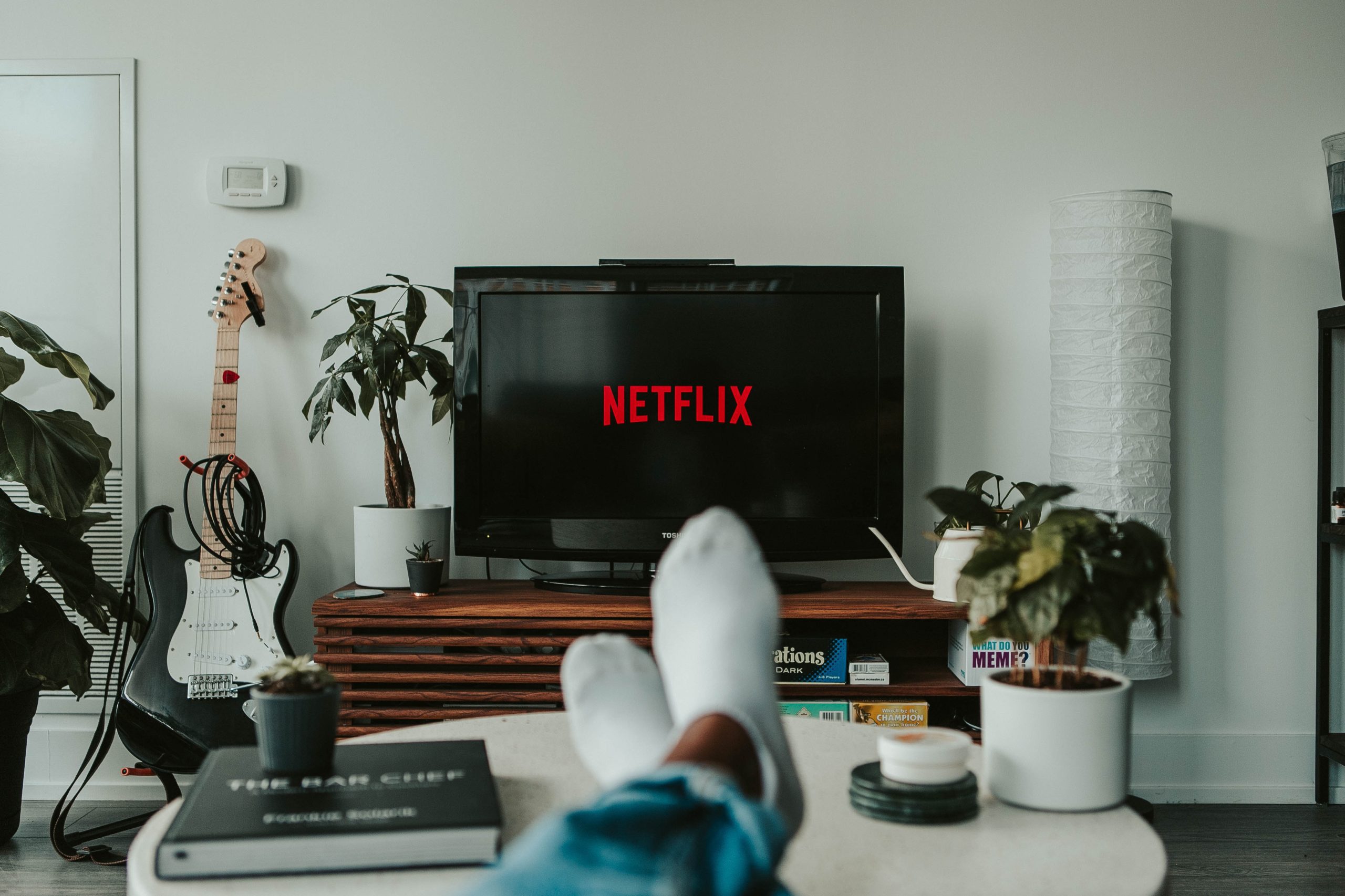 Man with feet on coffee table and a TV with Netflix logo in the background.