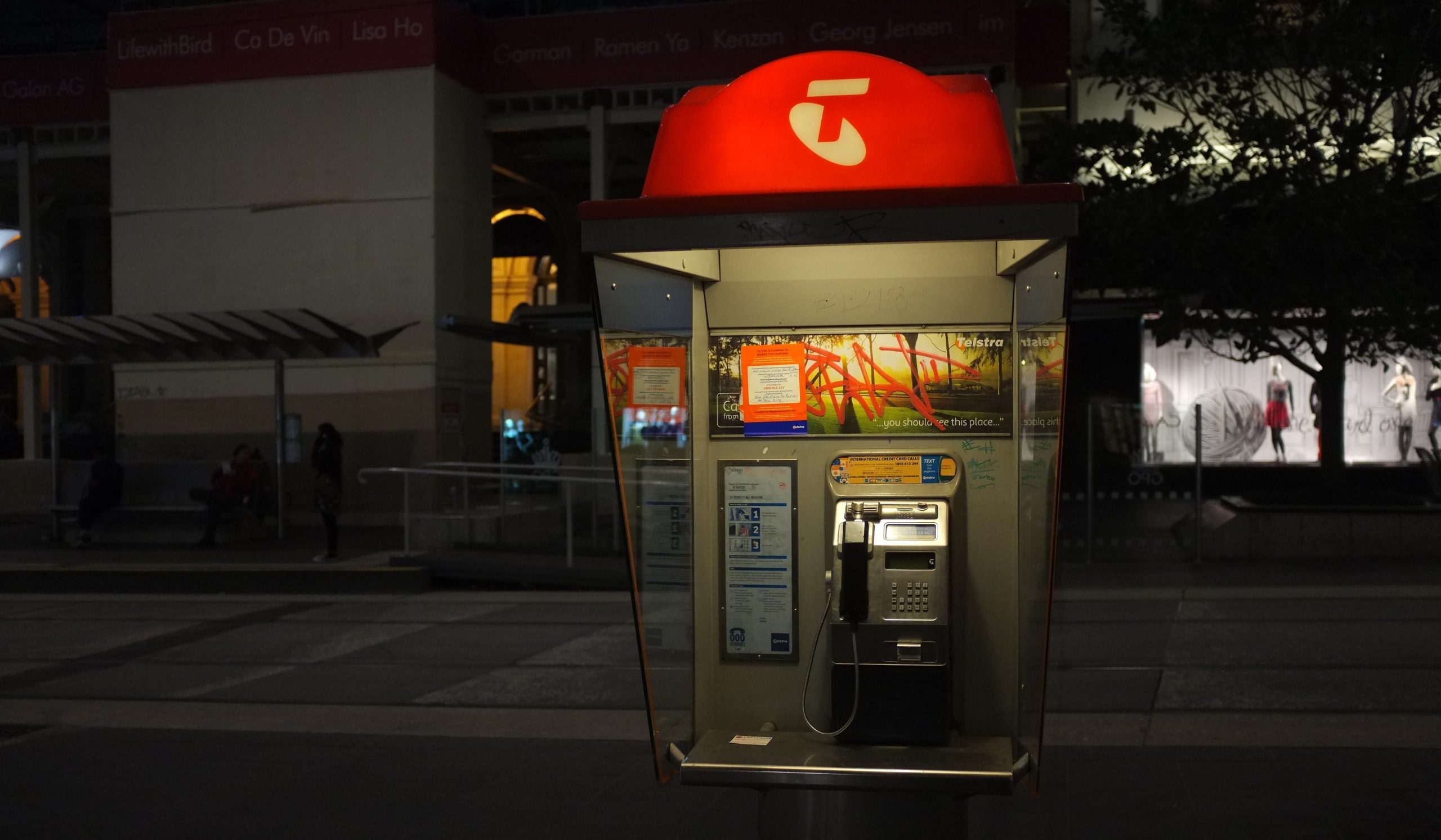 Telstra payphone lit up at night.