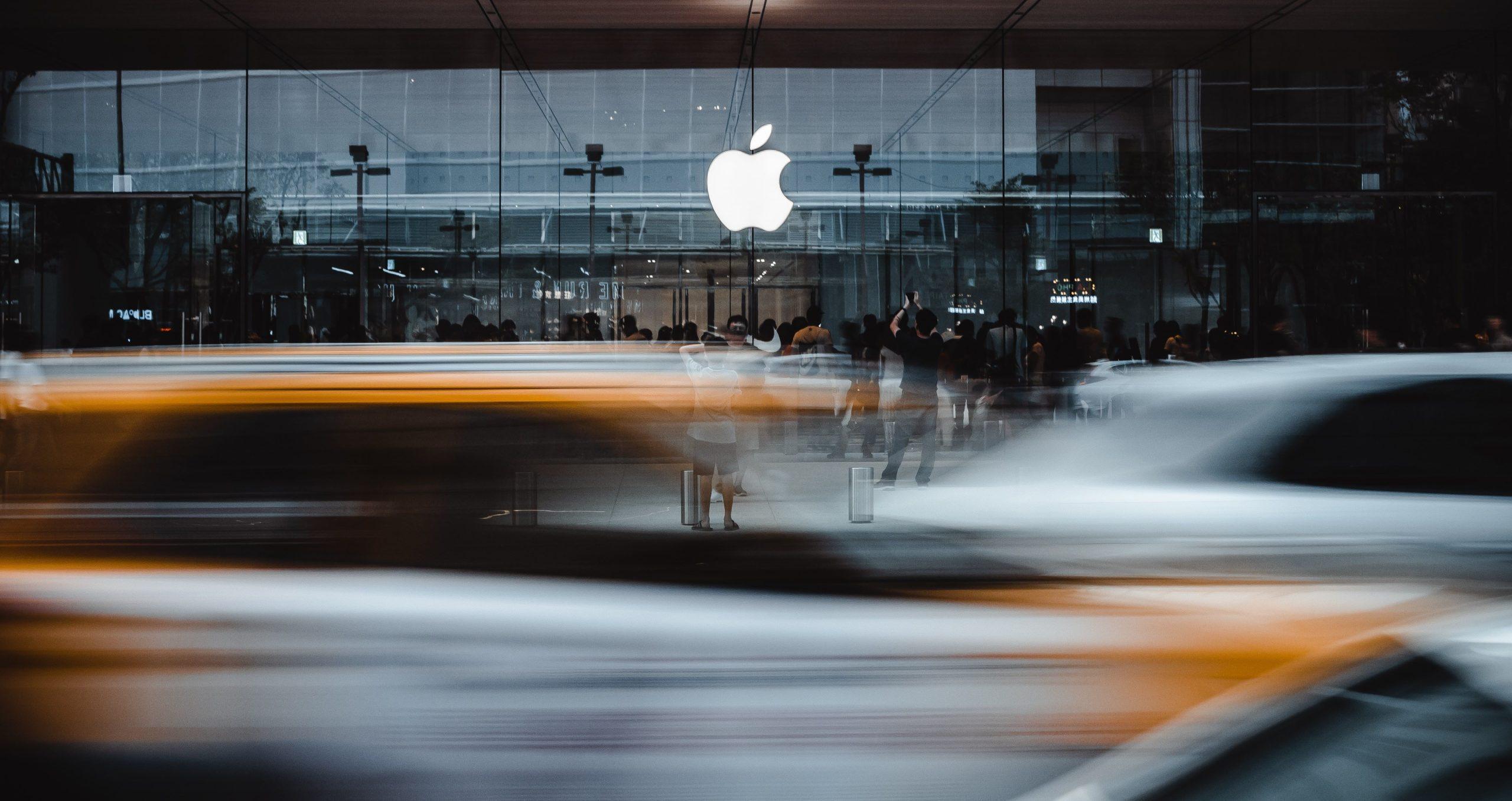 Apple logo on building facade in front of blurred traffic.