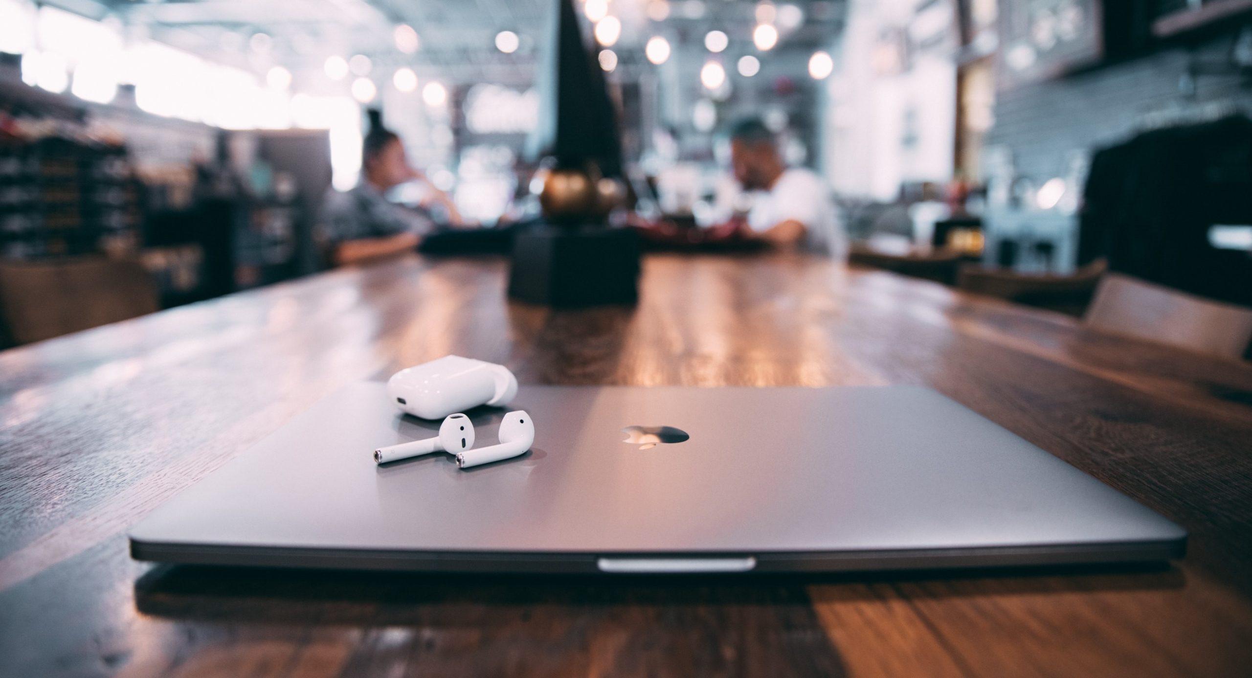 Laptop and AirPods placed on a wooden table against a blurred background.