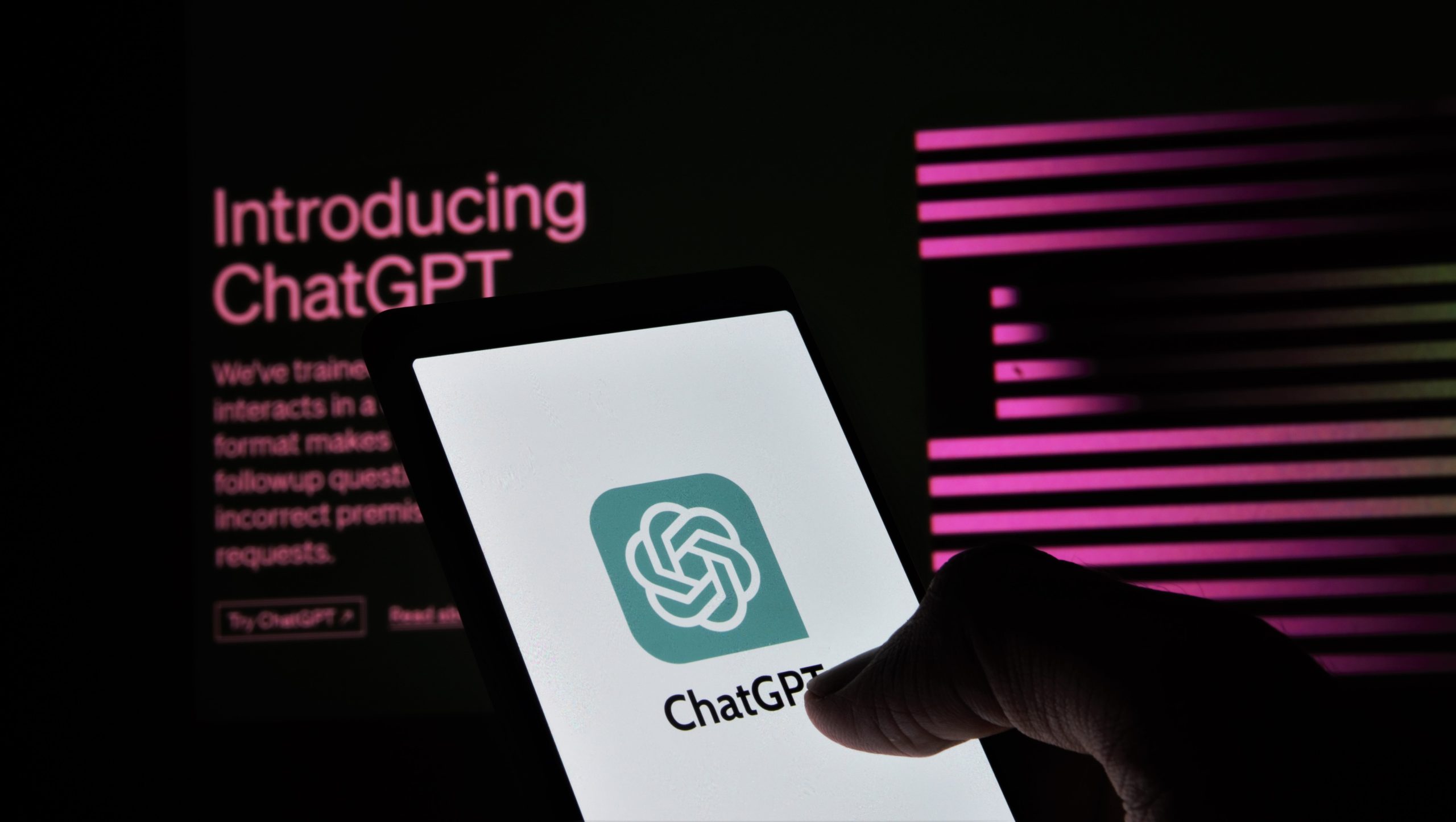 Smartphone displaying the ChatGPT logo against a backdrop of the ChatGPT homepage on a computer.