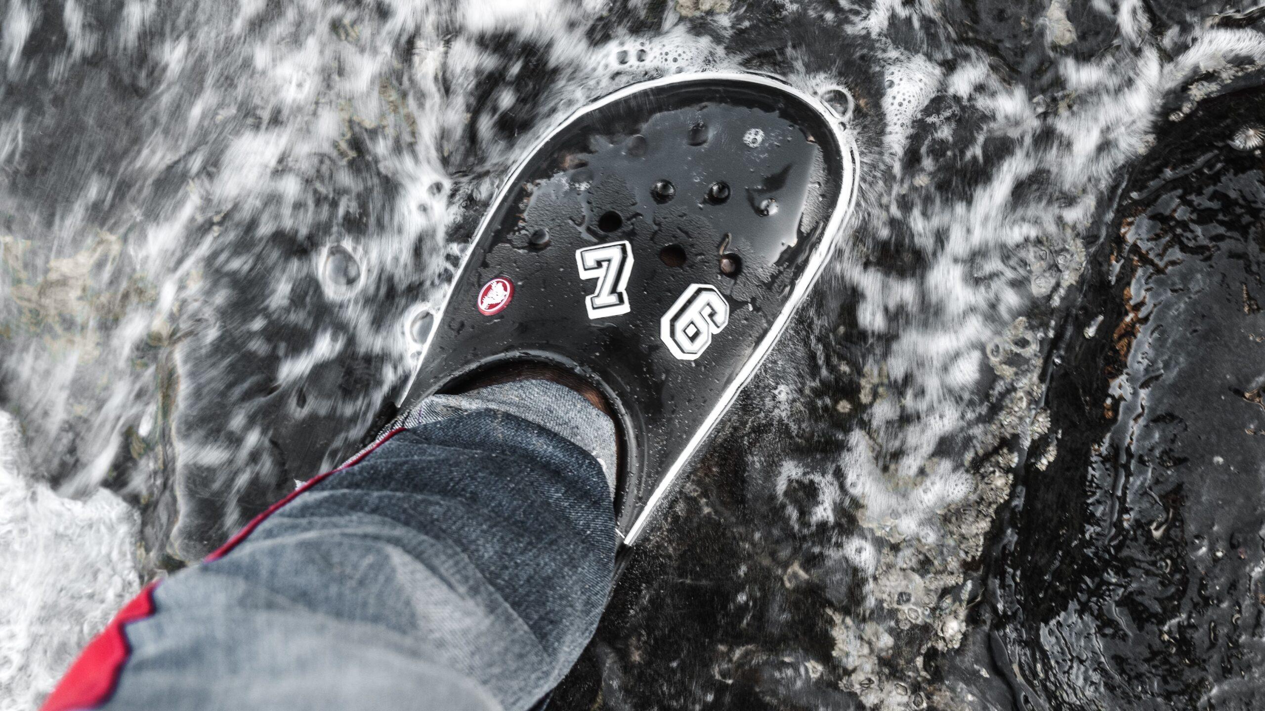 Close up of a black Crocs-branded shoe dangling over a rock face.