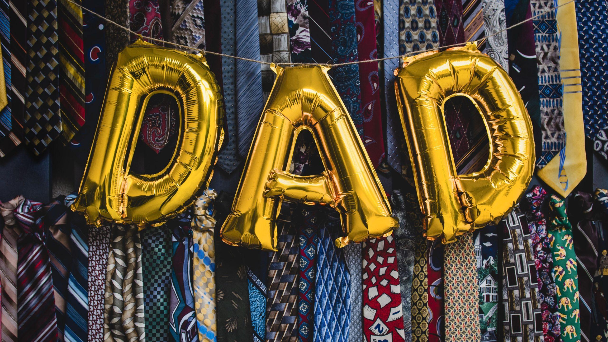 Giant party balloons spelling the word 'Dad' against a backdrop of neck ties.