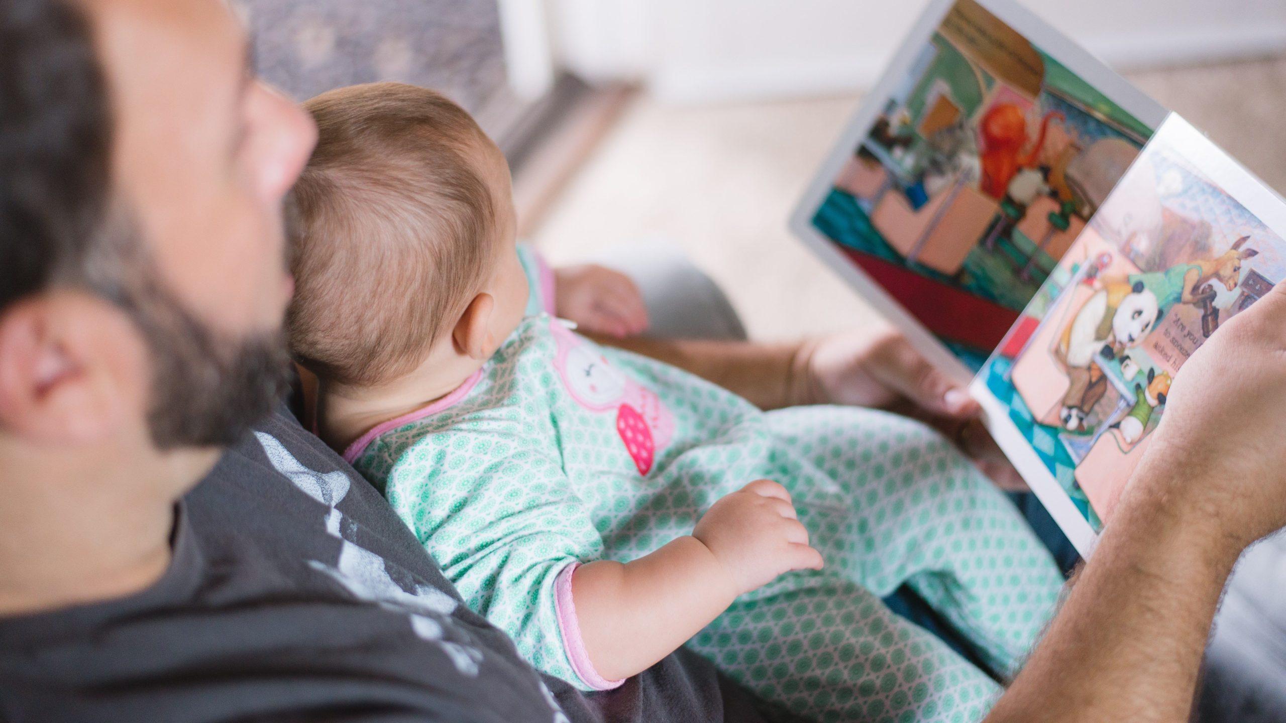 Man reading a children's book to a baby.