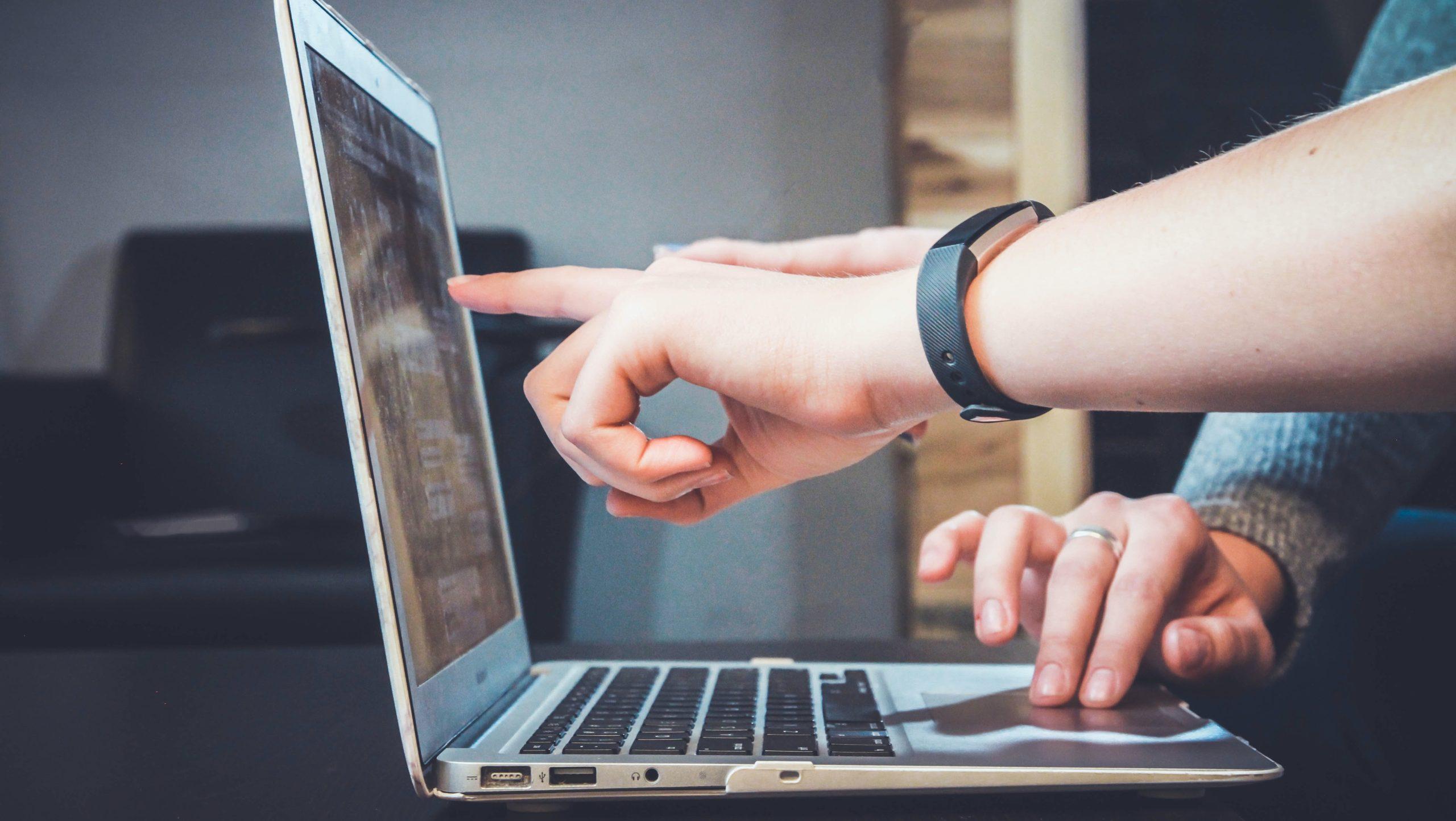 Person pointing at a laptop screen in front of another person.