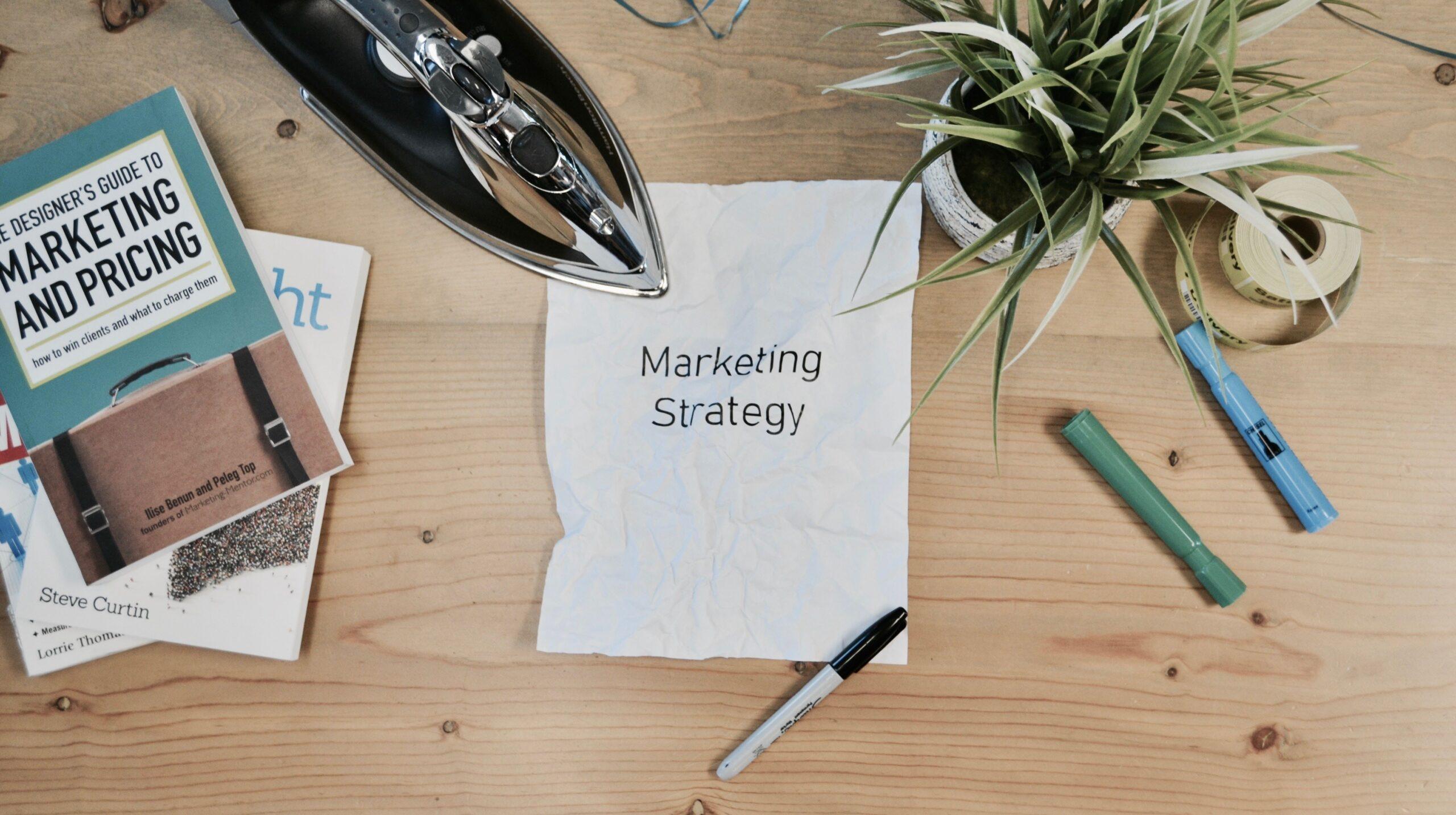 The words 'marketing strategy' written on a piece of paper, with an iron holding it held to a wooden surface.