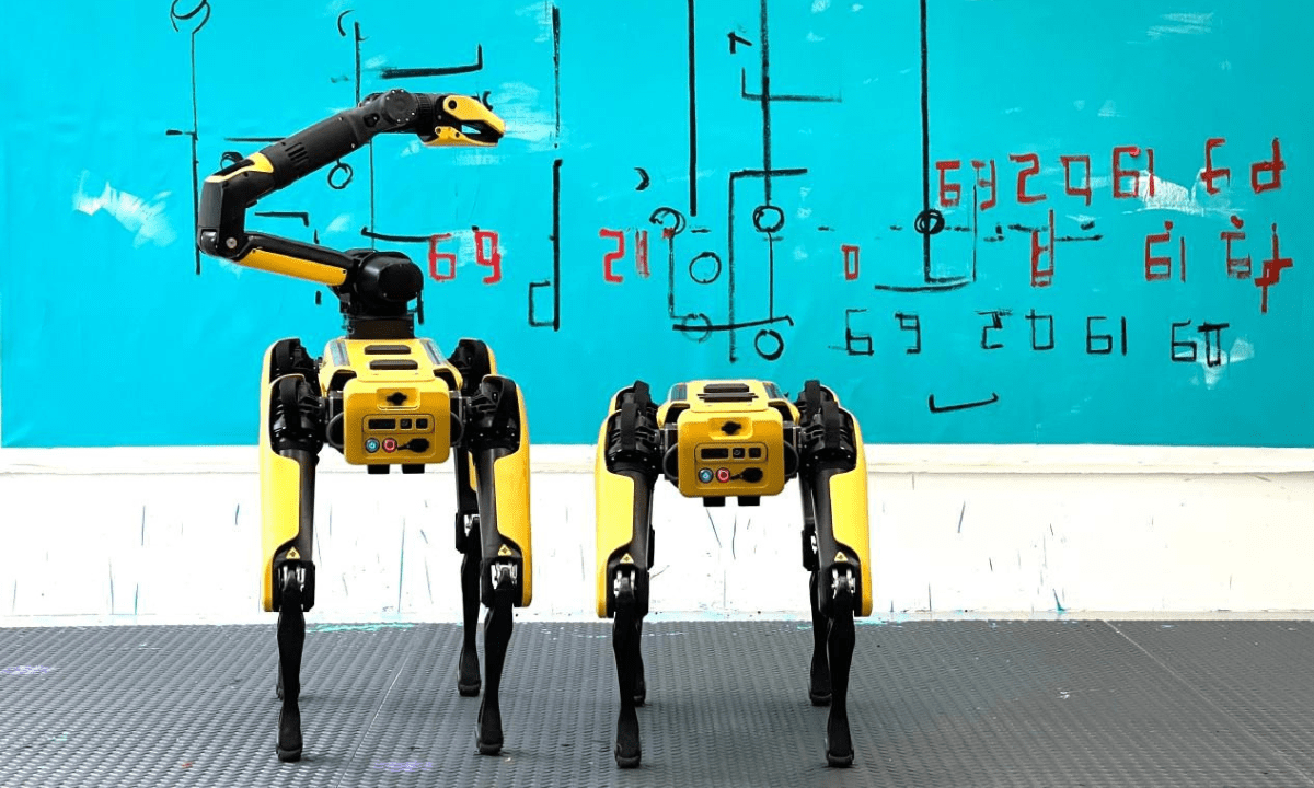 Two Boston Dynamics’ ‘Spot’ robot dogs stand in front of a canvas painting.