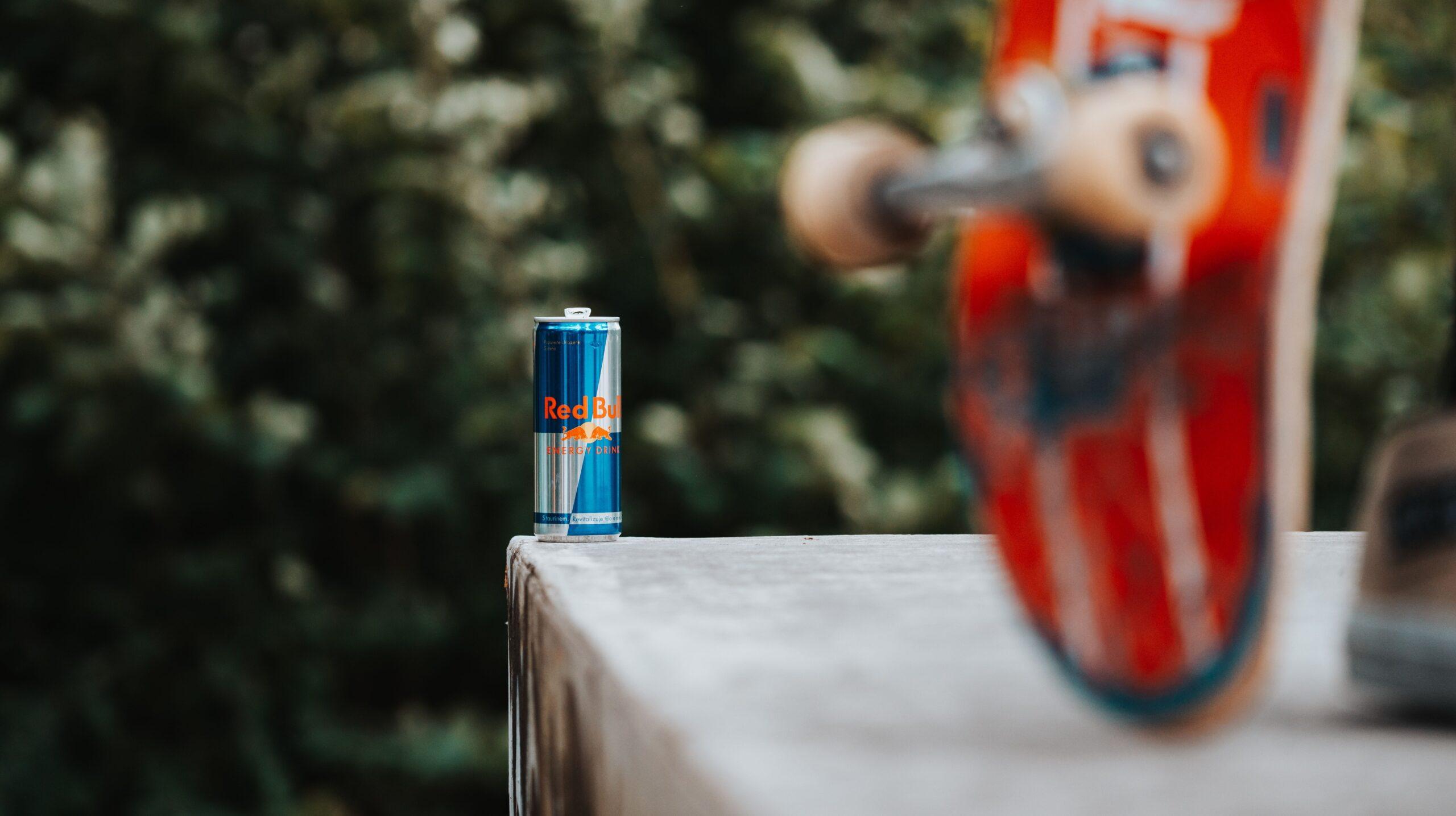 A Red Bull can on a ledge next to a skateboard.
