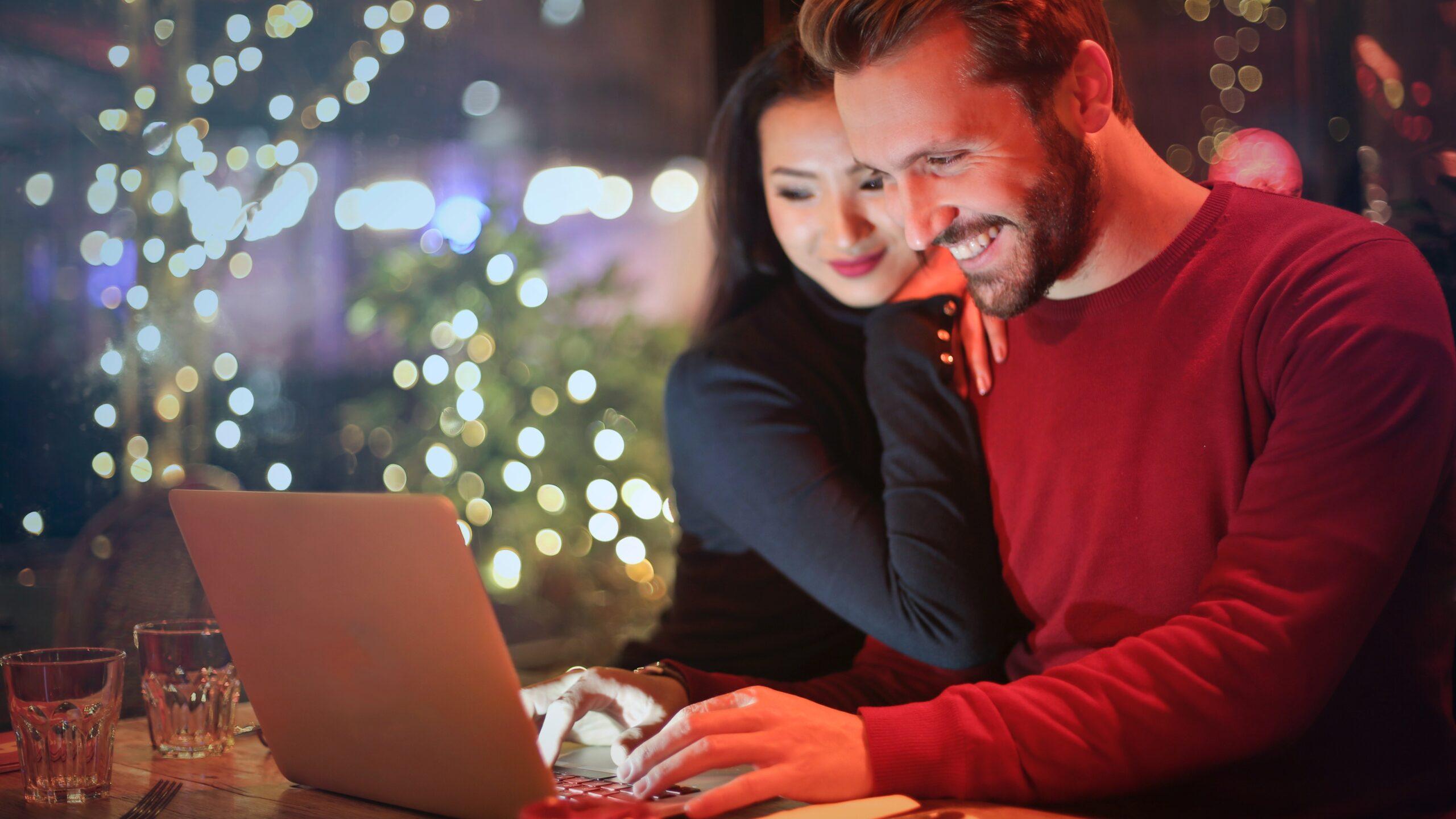 Man and a woman looking at a laptop in front of a blurred Christmas tree.