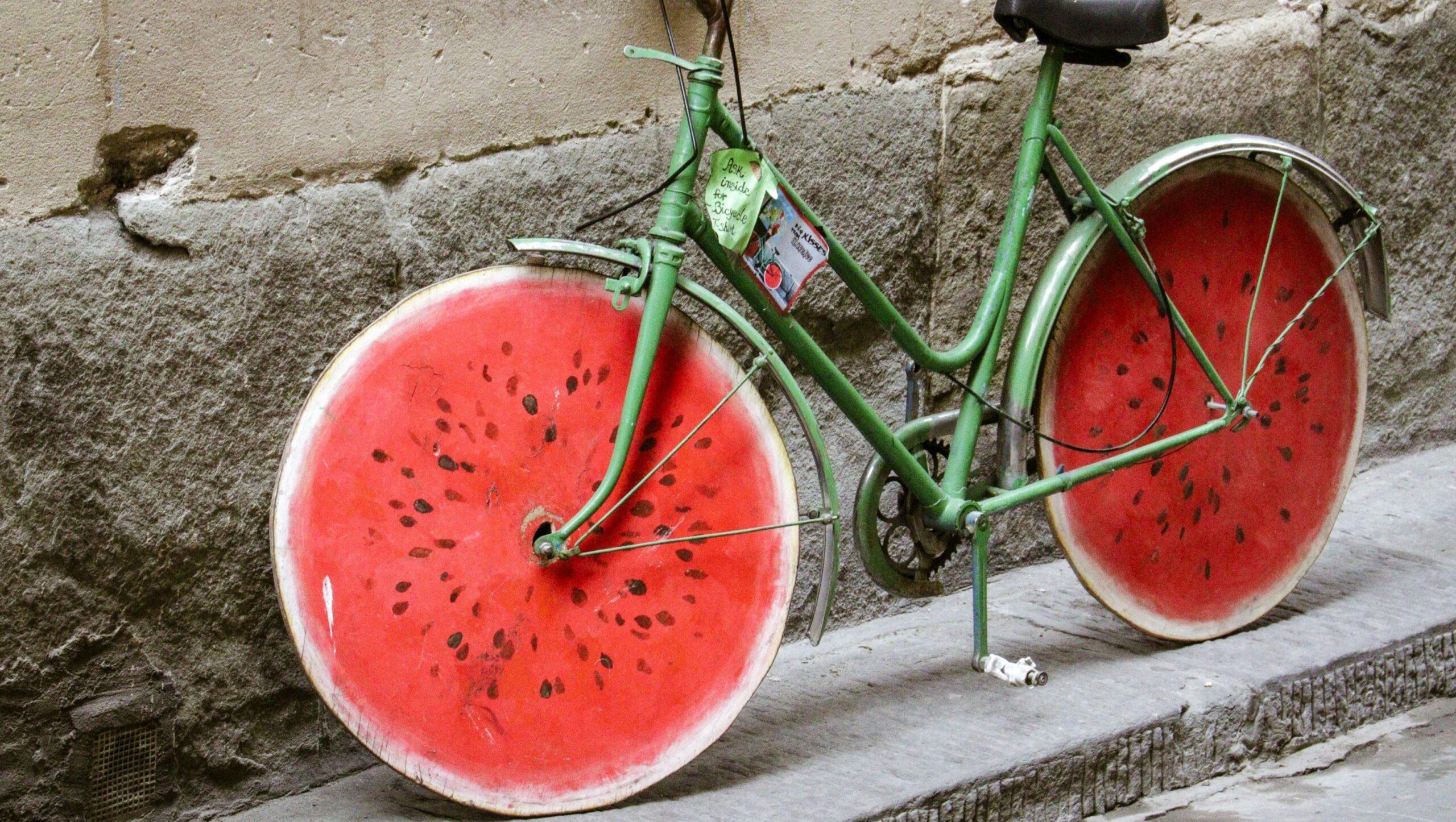 Green bike with watermelon-like wheels leaning up against a stone wall.