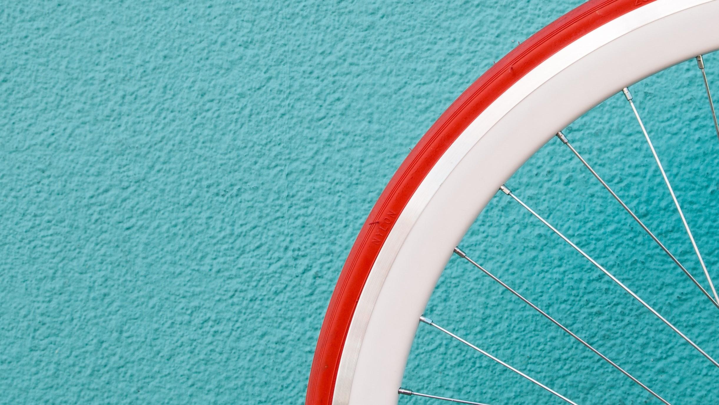 Part of a wheel of a bicycle against an aqua-coloured wall.