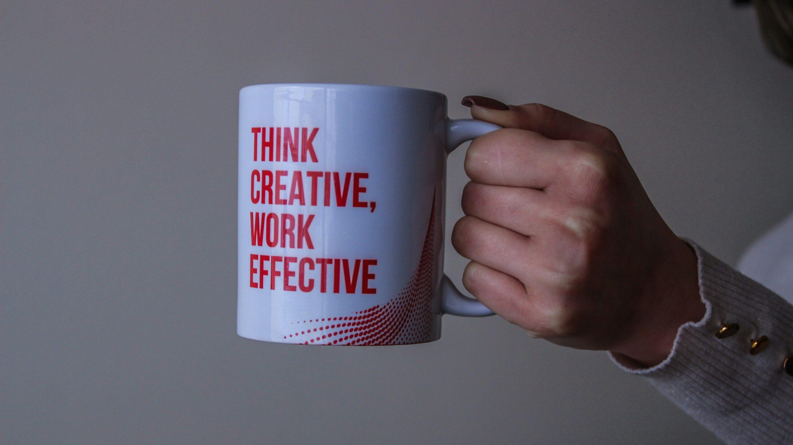 A close up of a person holding a coffee mug with the words 'think creative, work effective'.