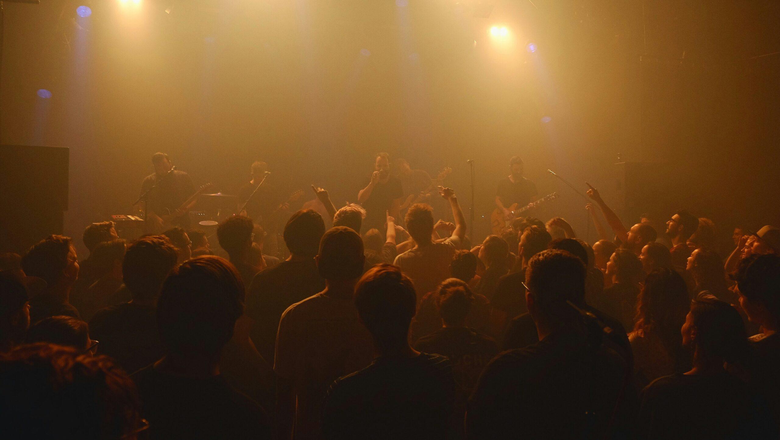 Crowd watching an unidentified musical band perform in a dimly lit venue.