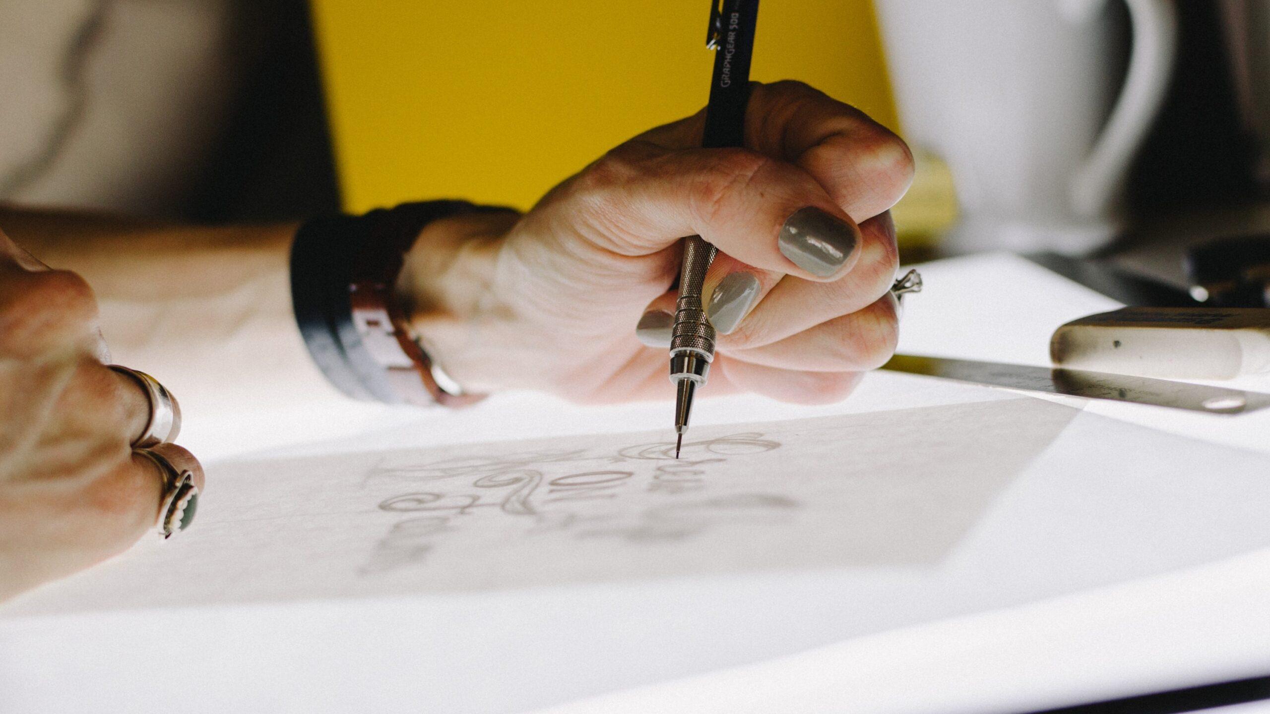 Close up of a person holding a drawing instrument to create an illustration or graphic on a piece of paper.