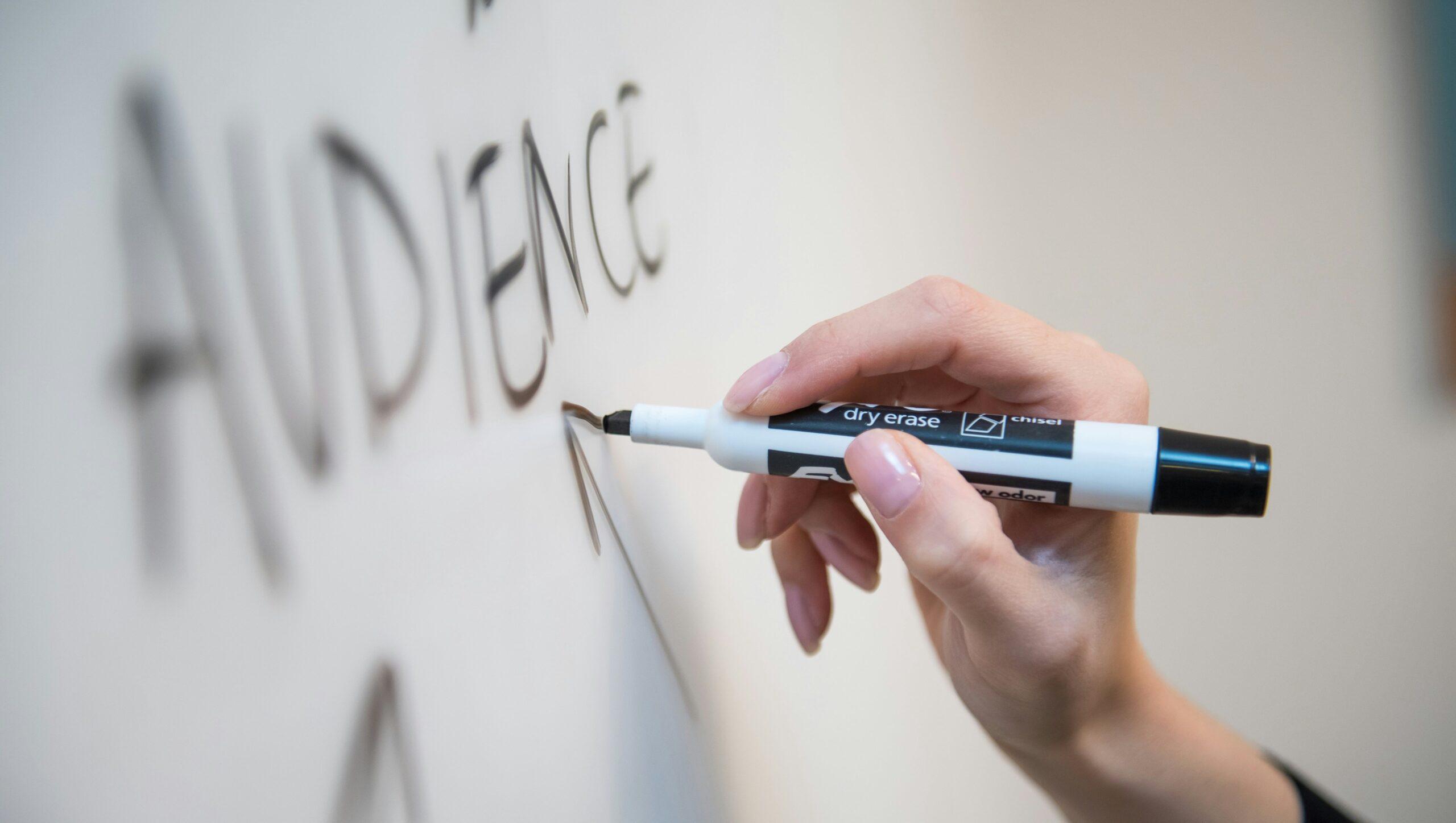 A close up of someone holding a marker to a whiteboard, drawing an arrow pointing to the word 'audience'.