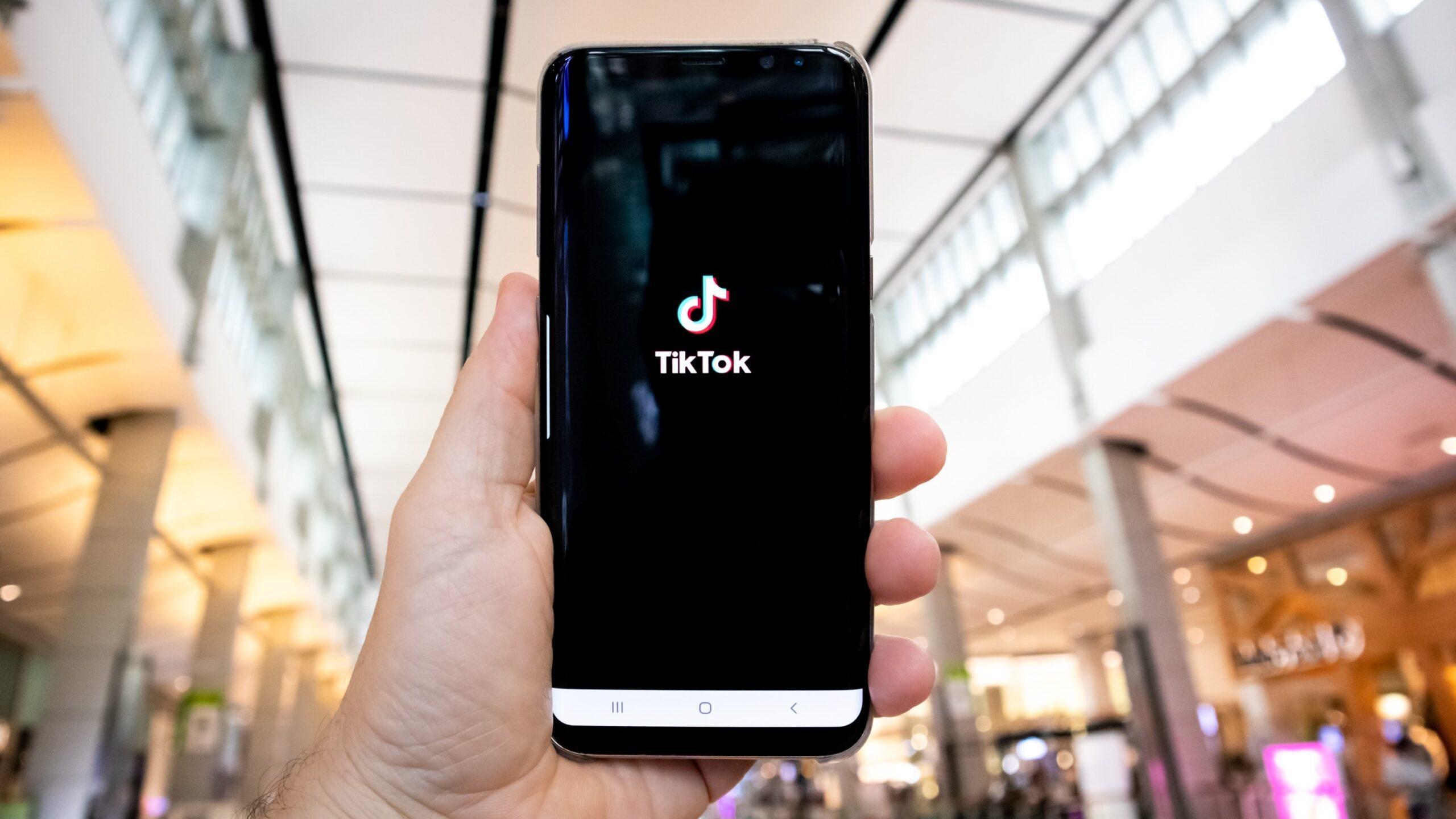 Close up of a hand holding a smartphone displaying the TikTok logo.