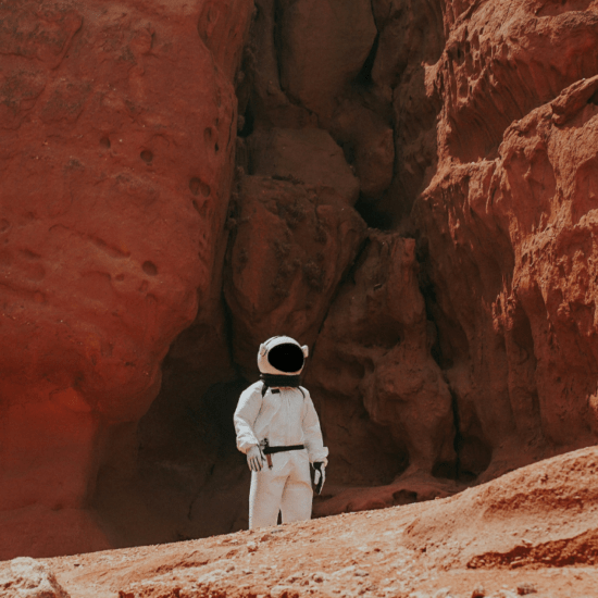 An astronaut standing on top of and surrounded by red rocks as part of an article about openings for a simulated Mars mission with NASA.