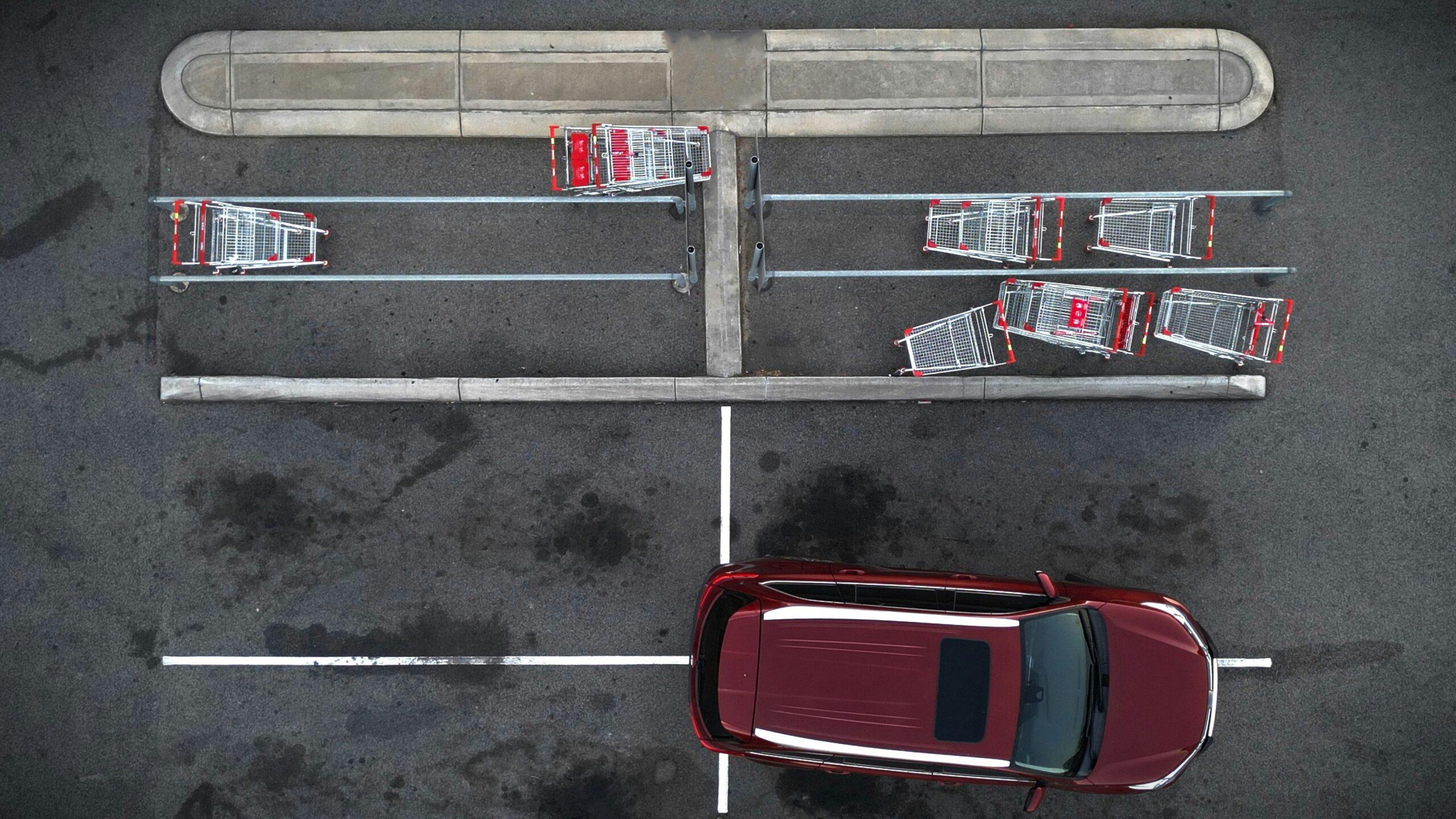 Aerial of a maroon-coloured car parked across several parking spots in a car park complete with shopping trolleys.