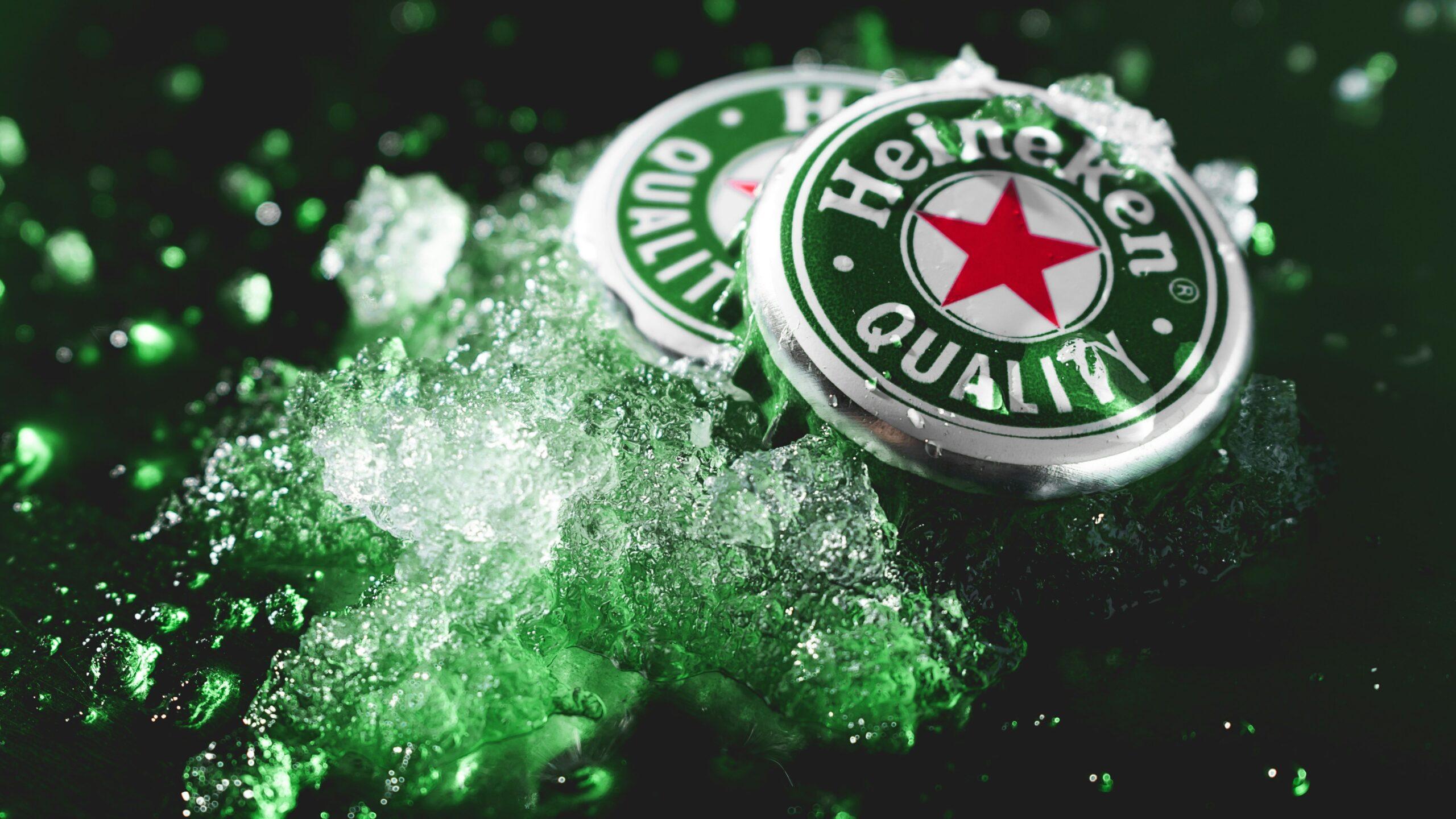 Two Heineken beer bottle tops placed upright on crushed ice.