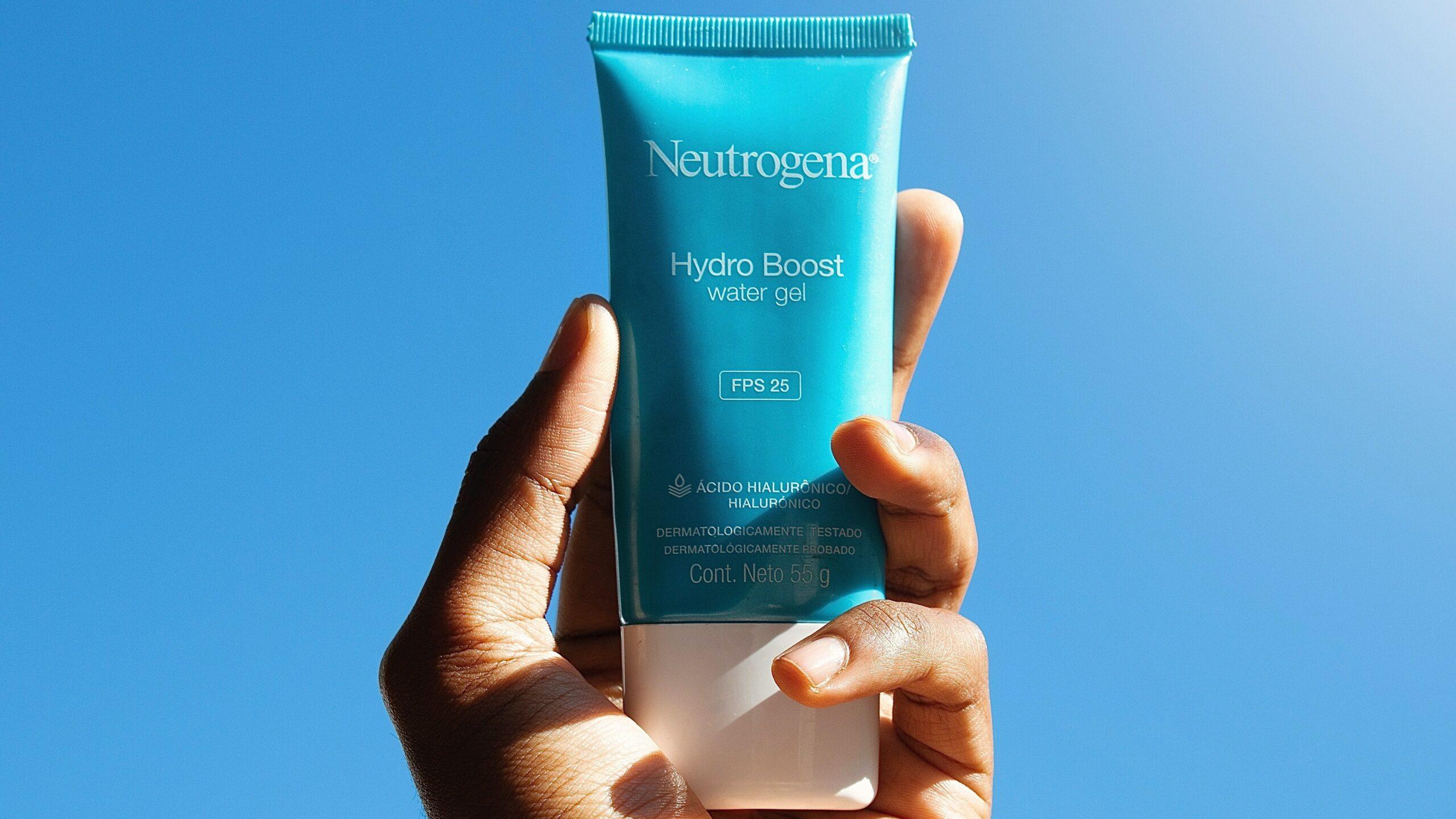 Close up of a hand holding a bottle of Neutrogena water gel against a backdrop of blue sky.
