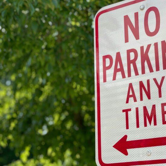Close up of a street sign that reads 'no parking any time' against a backdrop of trees as part of an article about Chinese tech to combat illegal parking.