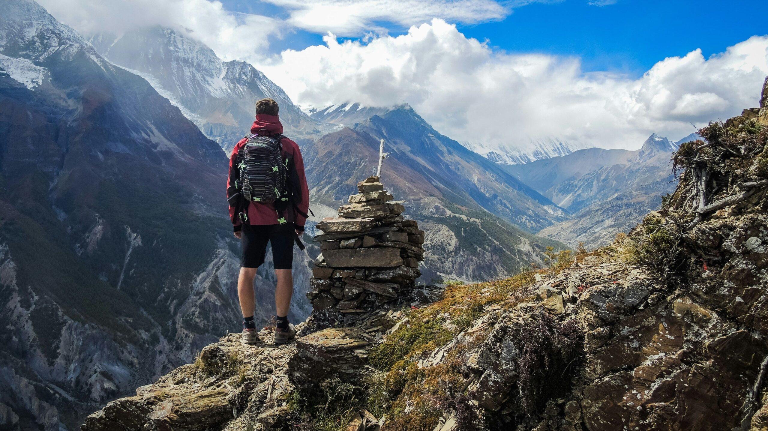 Person standing on a craggy mountain looking across at a view of more mountains within the Manang Valley in Nepal. 