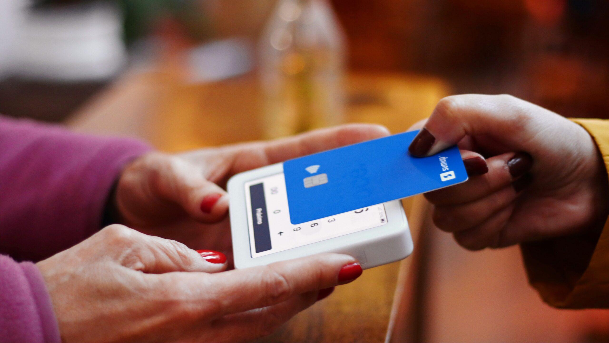 Close up of someone holding a debit or credit card while someone else holds a portable card-reading device.